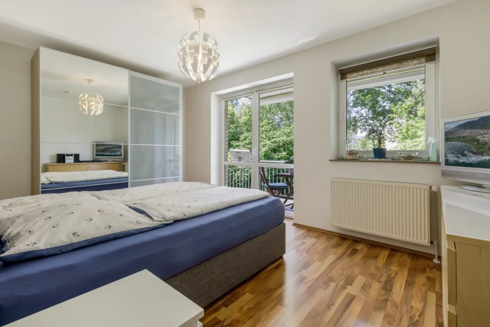 Helles Schlafzimmer mit großem Bett, Kleiderschrank und Fenster mit Blick ins Grüne.