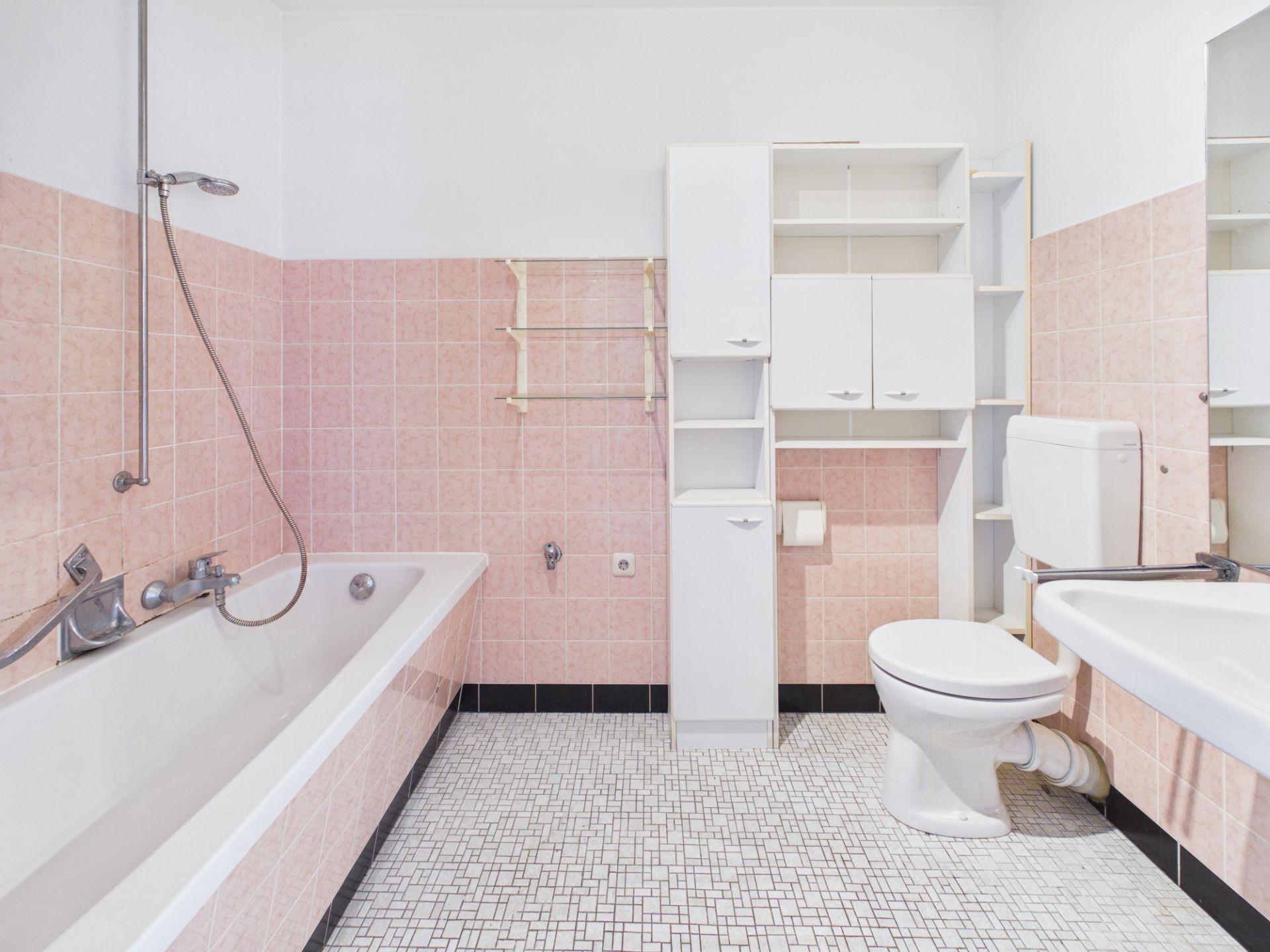 Helles Bad mit rosa Fliesen, Badewanne, Toilette, Waschbecken und weißen Schränken.