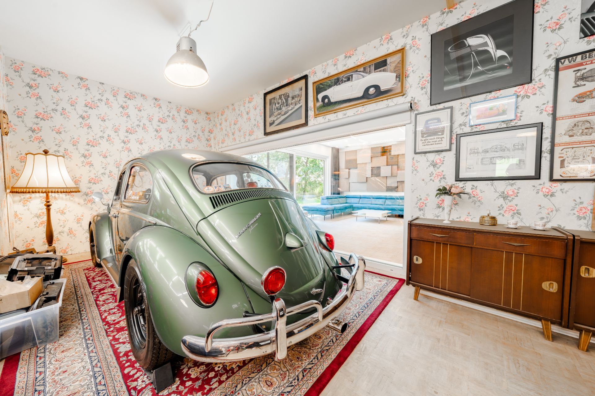 Grüner Oldtimer steht auf Teppich in Wohnzimmer, mit Bildern an der floral tapezierten Wand.