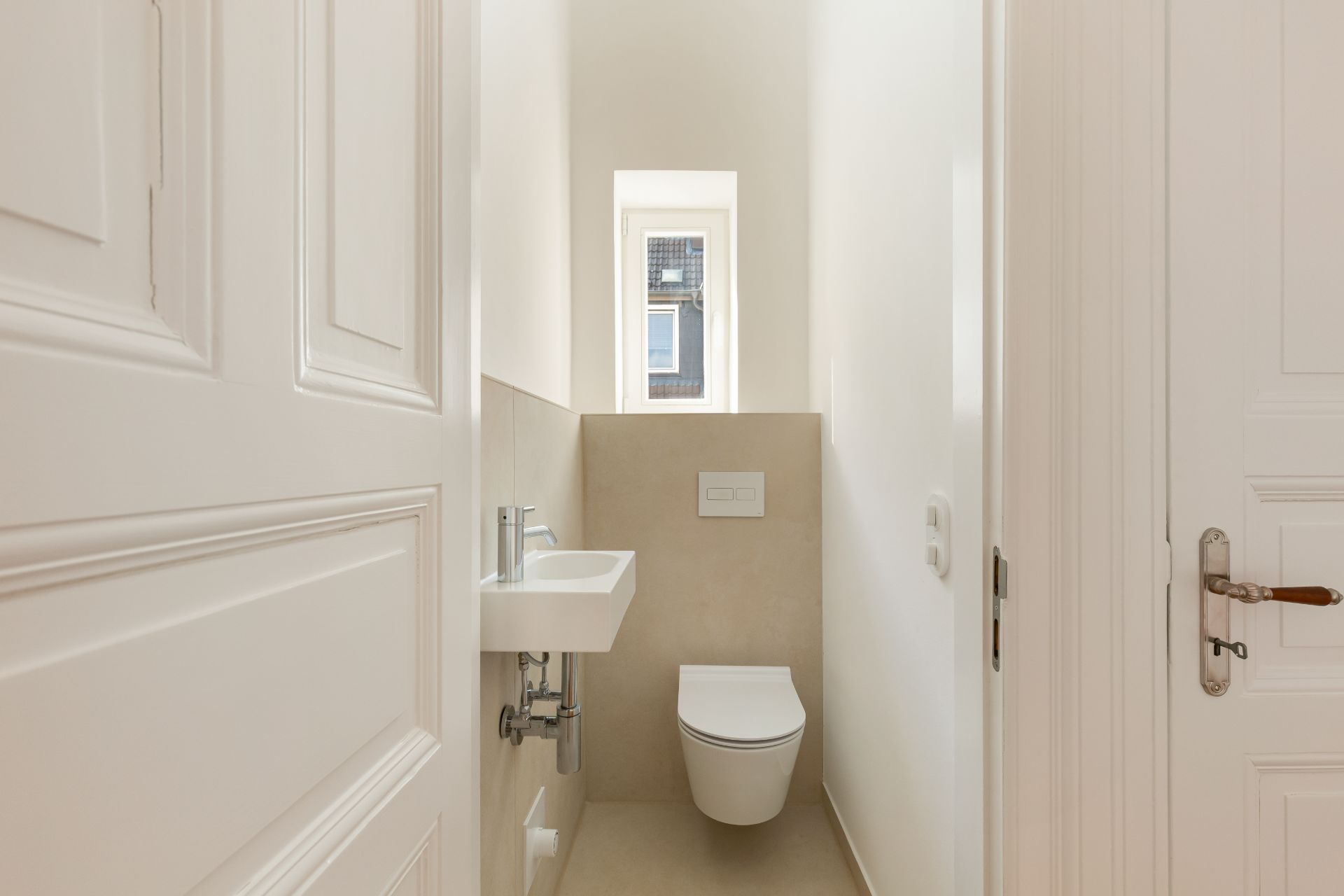 Kleines, helles Gäste-WC mit Wandtoilette, kleinem Waschbecken und Fenster.
