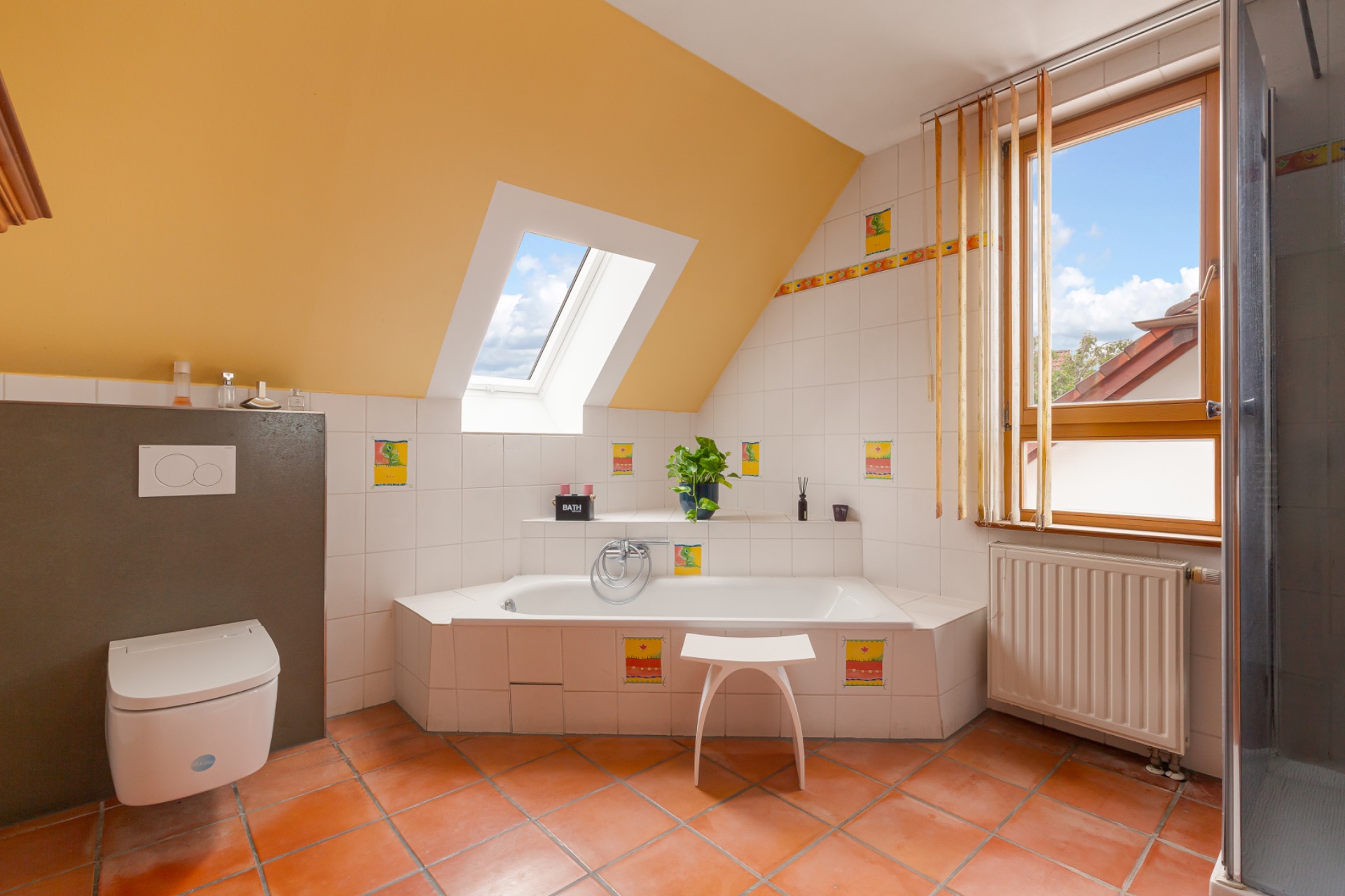 Helles Badezimmer mit Badewanne, WC, Fenster, Dachfenster und Fliesenboden.