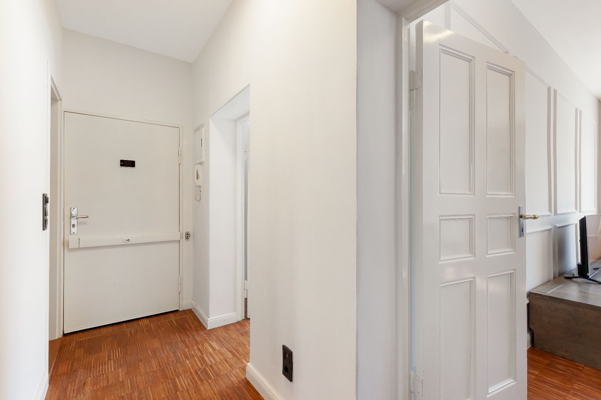 Heller Flur mit Holzboden, weißen Türen und Wänden in einer Wohnung.