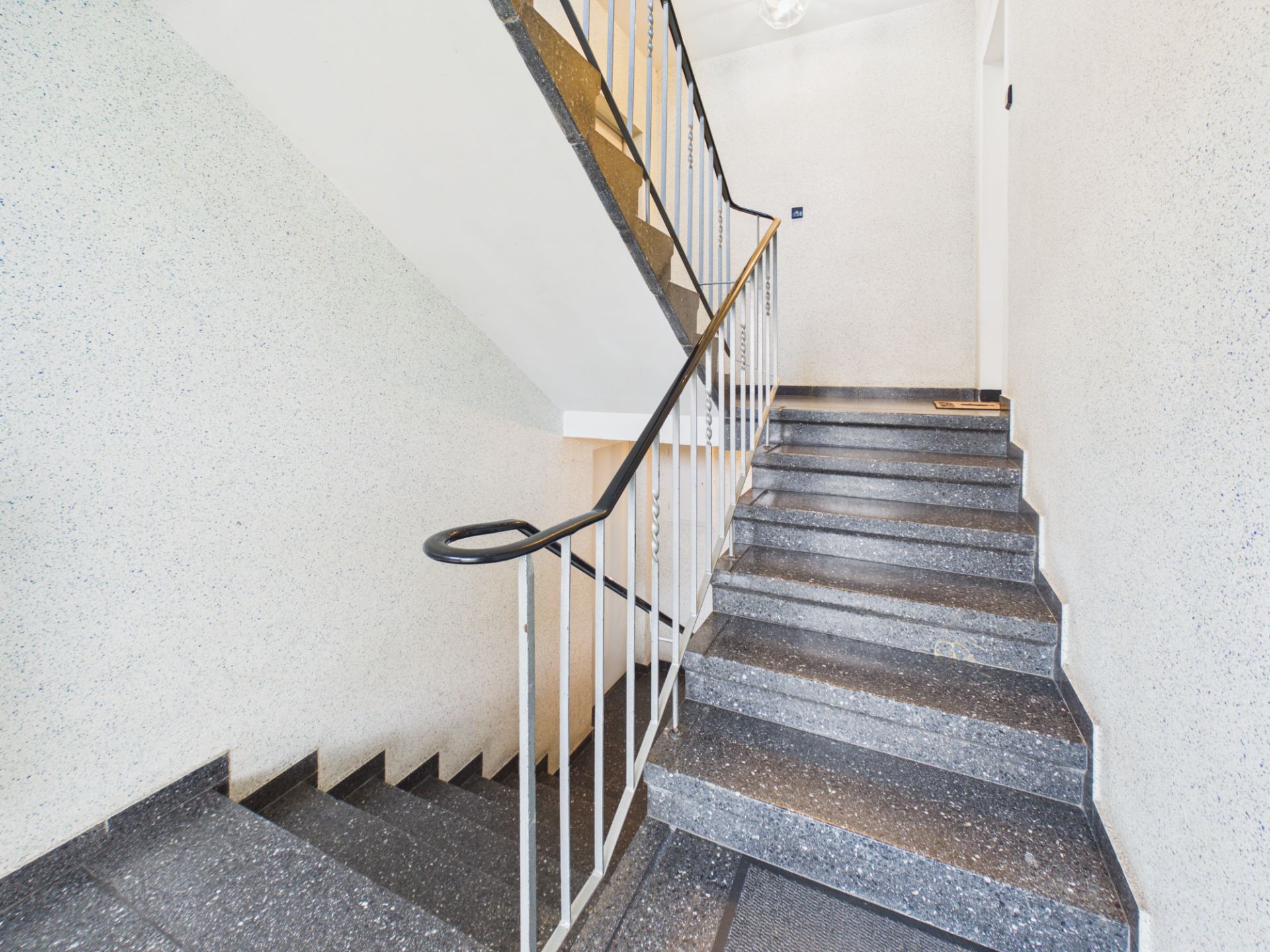 Helles Treppenhaus mit grauen Stufen und weißem Geländer in einem Wohngebäude.