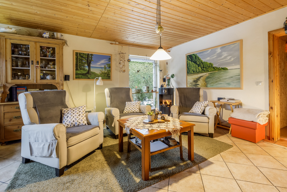 Gemütliches Wohnzimmer mit drei Sesseln, Holztisch, Teppich und Bildern an der Wand.