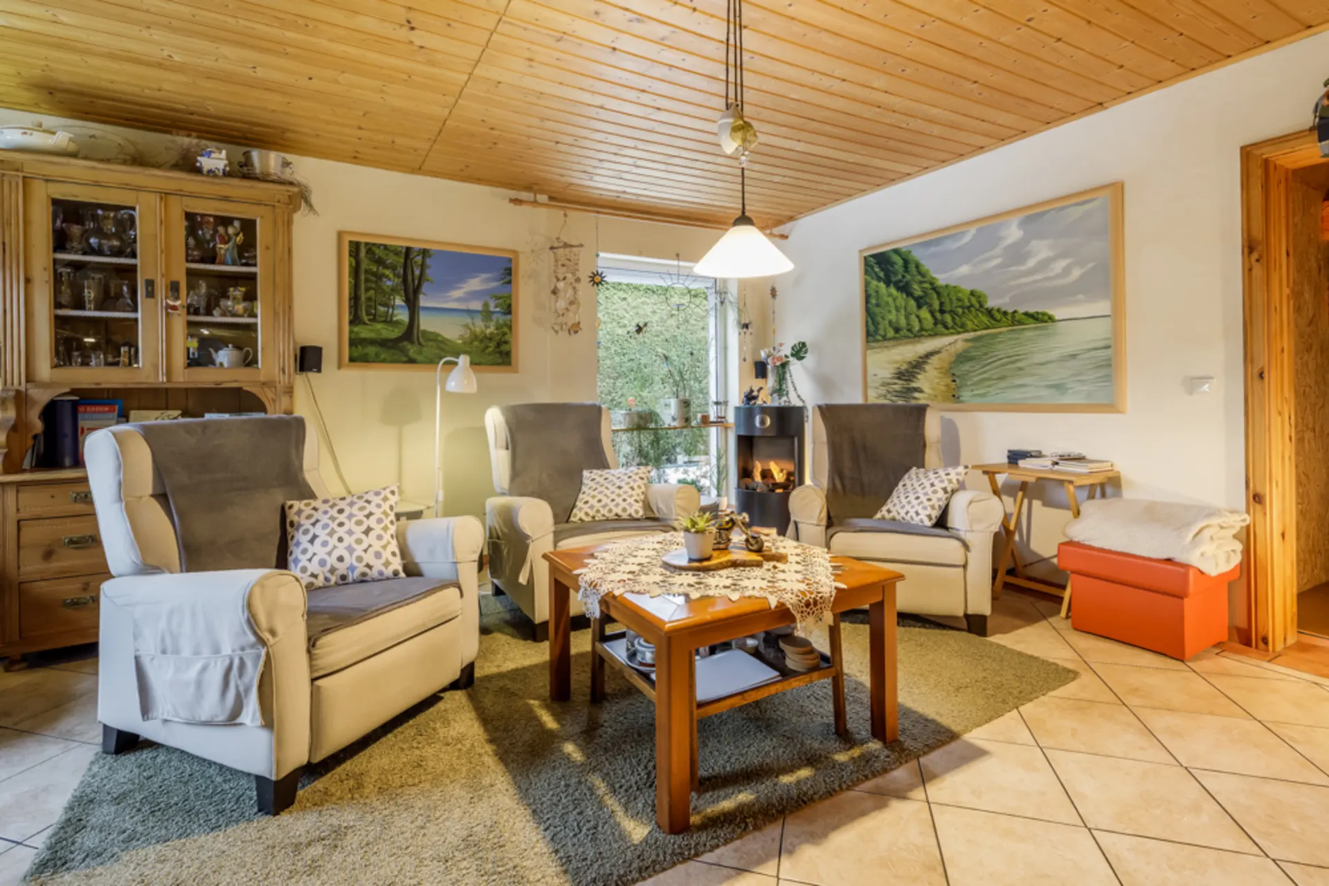 Gemütliches Wohnzimmer mit drei Sesseln, Holztisch, Teppich und Bildern an der Wand.