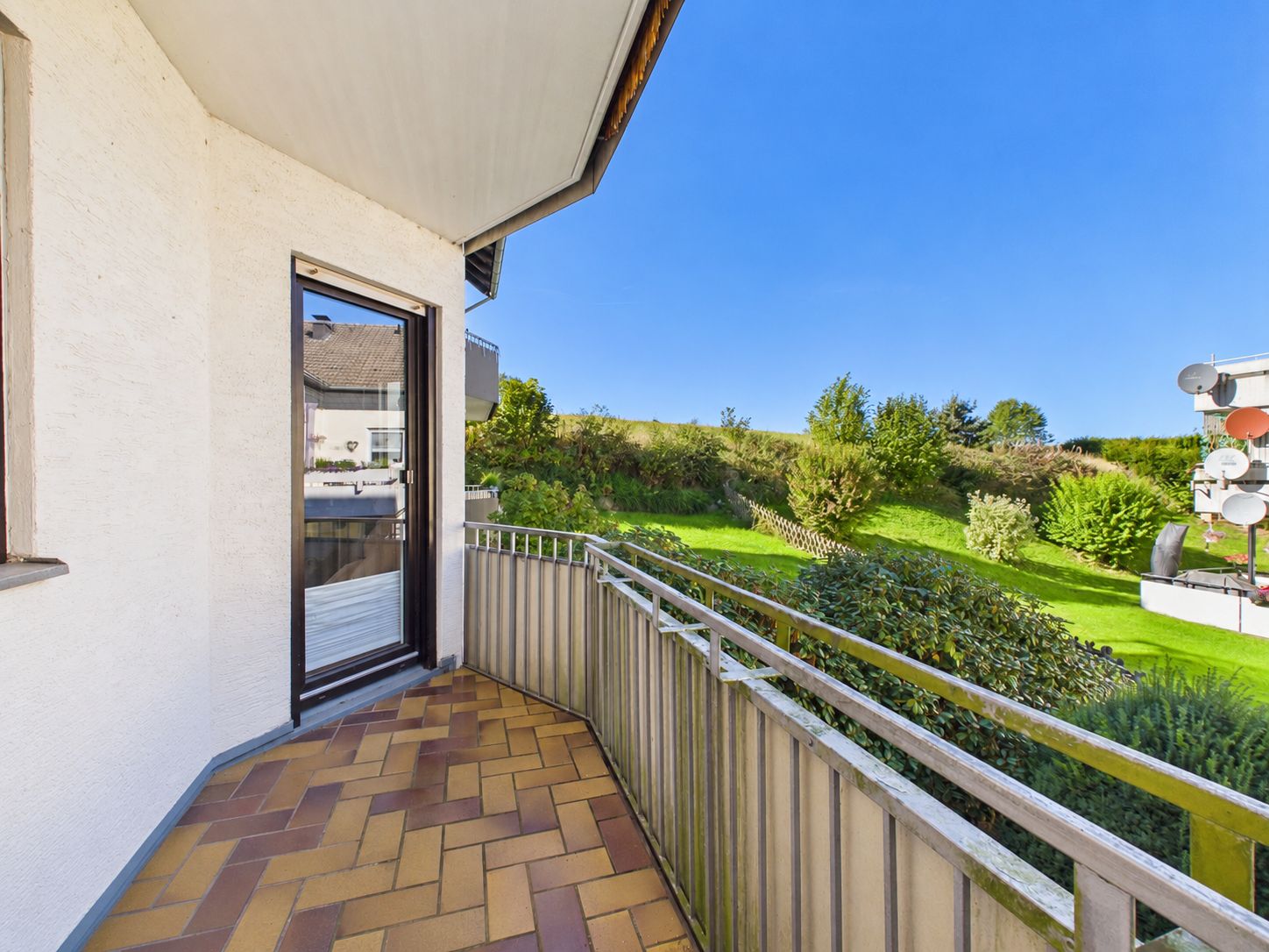 Balkon mit Fliesenboden, Metallgeländer und Blick auf einen grünen Garten.