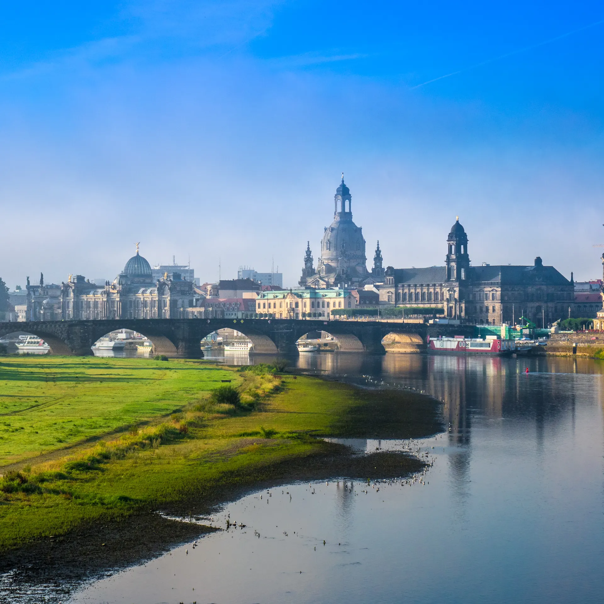 Stadtansicht mit Fluss, Brücke und historischen Gebäuden im Hintergrund.