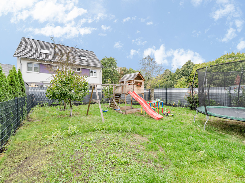 Garten mit Spielplatz, Rutsche, Schaukel, Baumhaus und Trampolin, von Zaun umgeben.