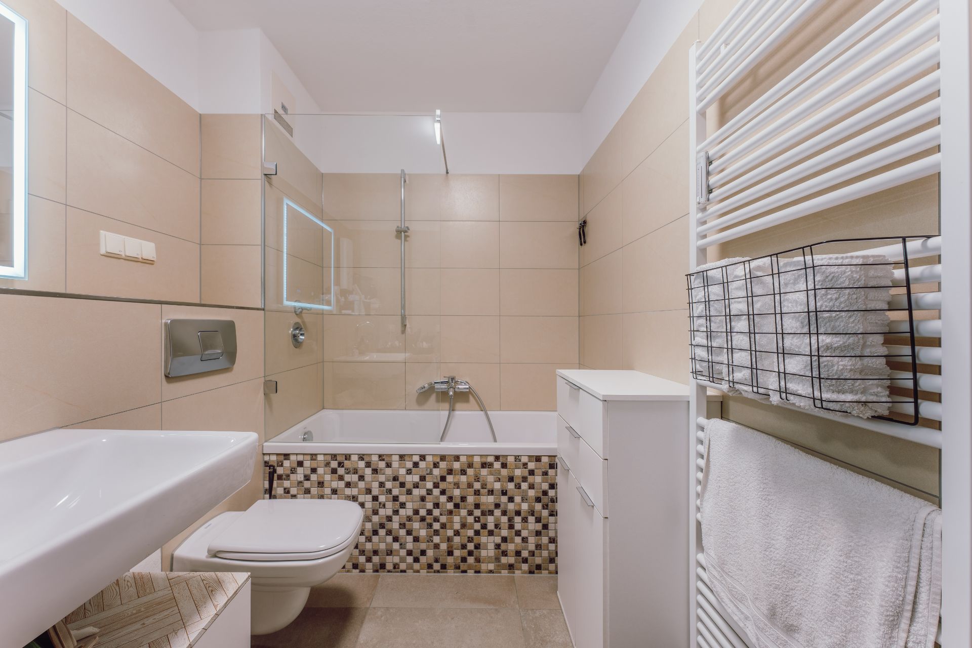 Modernes Badezimmer mit Badewanne, Waschbecken, WC, Handtuchheizung und weißen Handtüchern.