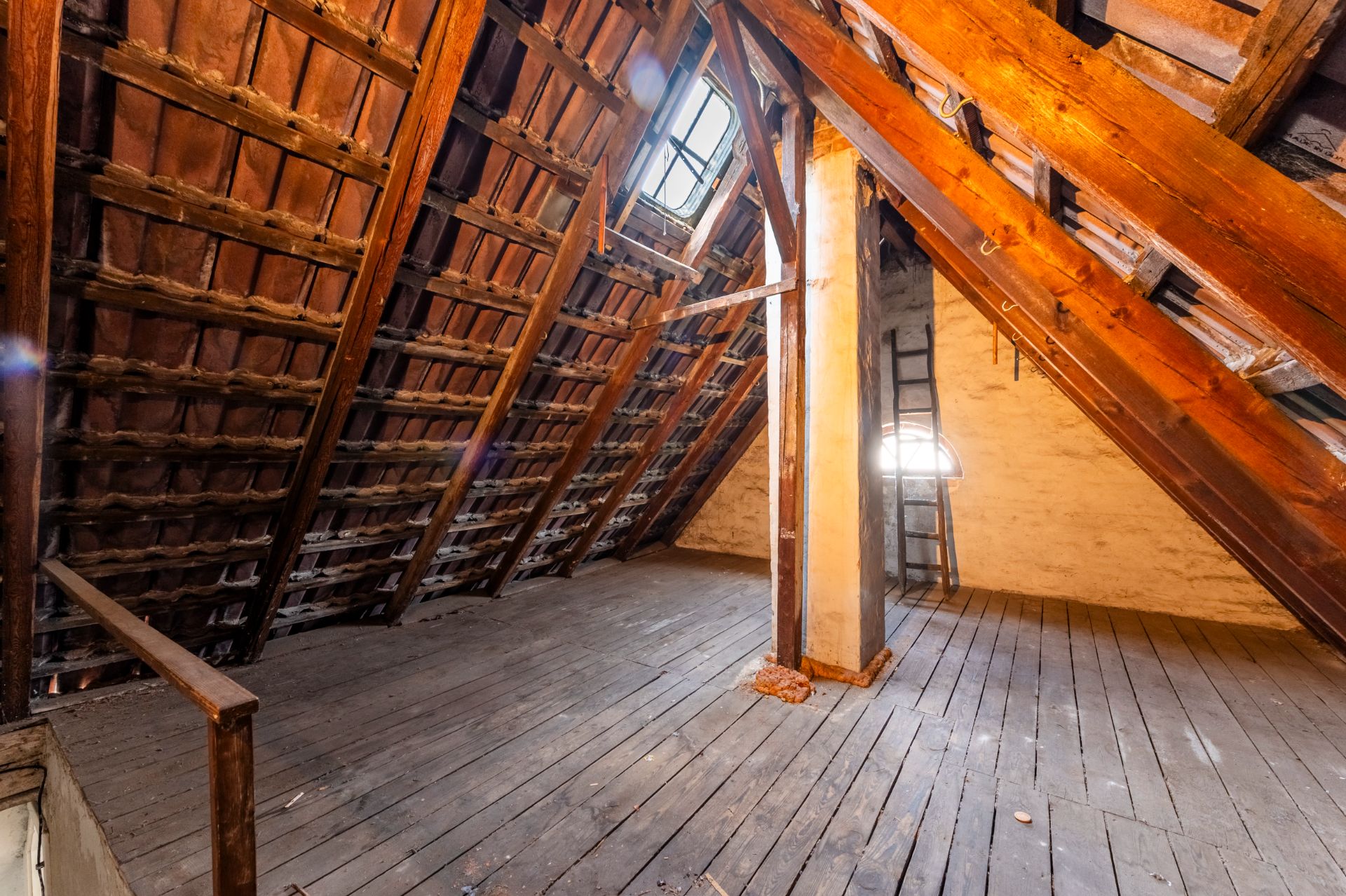 Dachboden mit Holzfußboden, Schrägdach, Fenster und einer Leiter an der Wand.