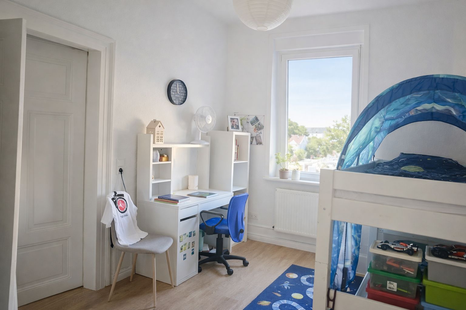 Helles Kinderzimmer mit Hochbett, Schreibtisch, Stuhl und Fenster mit Blick nach draußen.