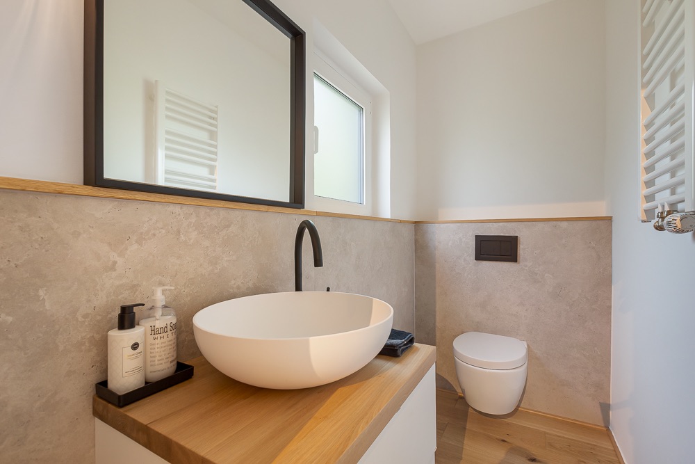 Modernes Badezimmer mit rundem Waschbecken, Spiegel, Fenster und wandhängender Toilette.