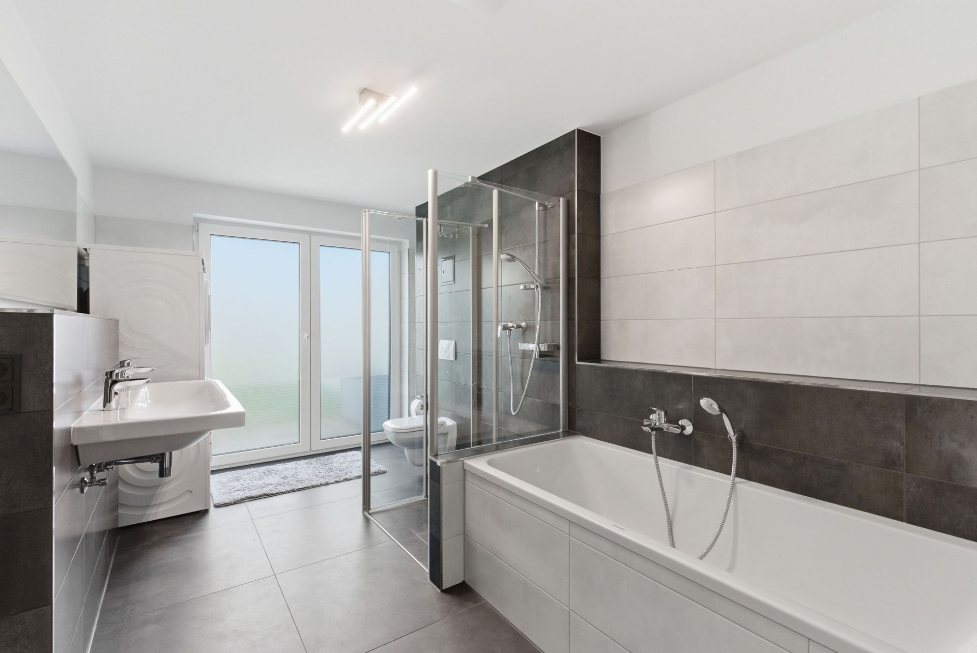 Modernes Badezimmer mit Badewanne, Dusche, Doppelwaschbecken und großer Fenstertür.
