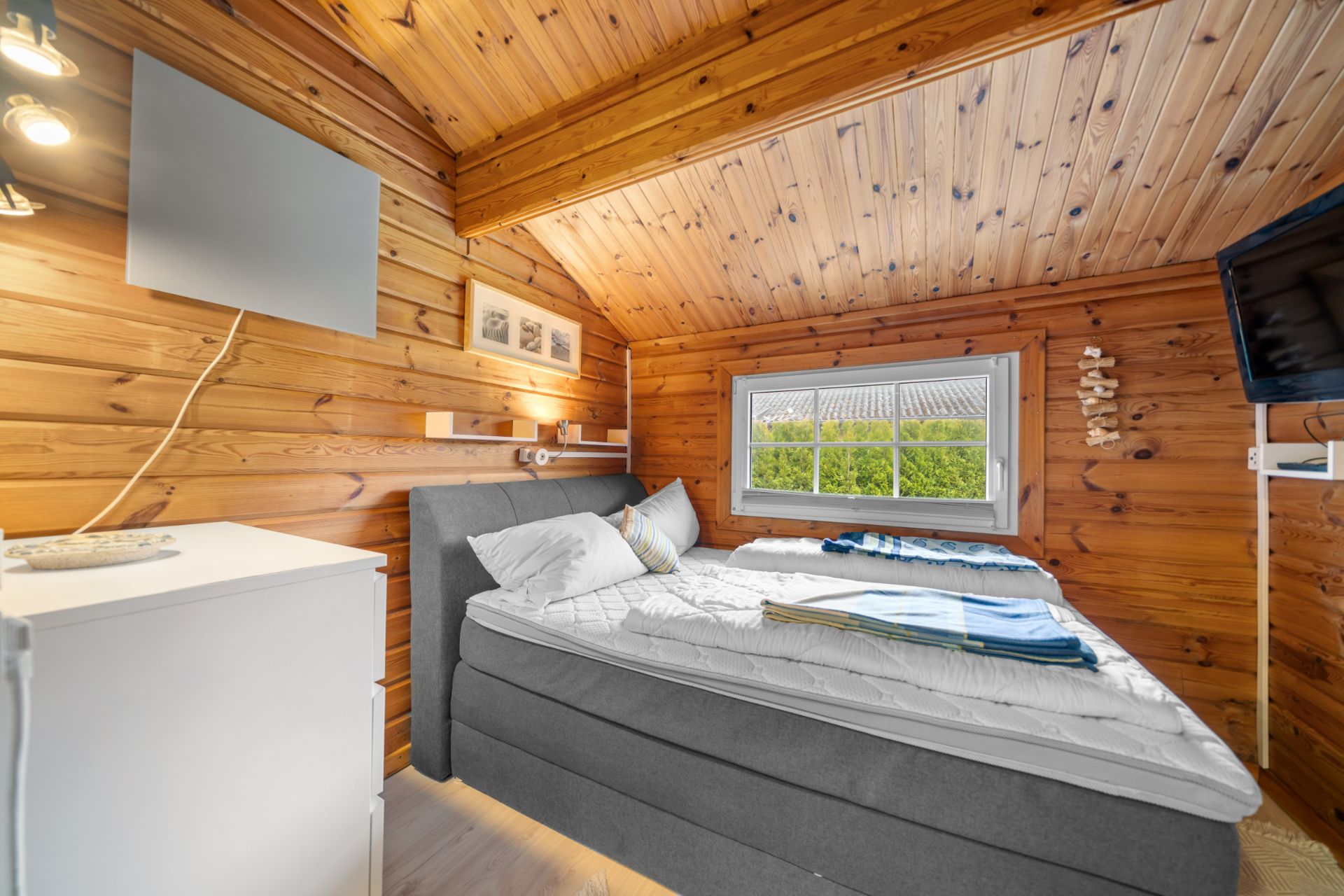 Kleines Schlafzimmer mit Holzwänden, Doppelbett, Fenster und Fernseher.