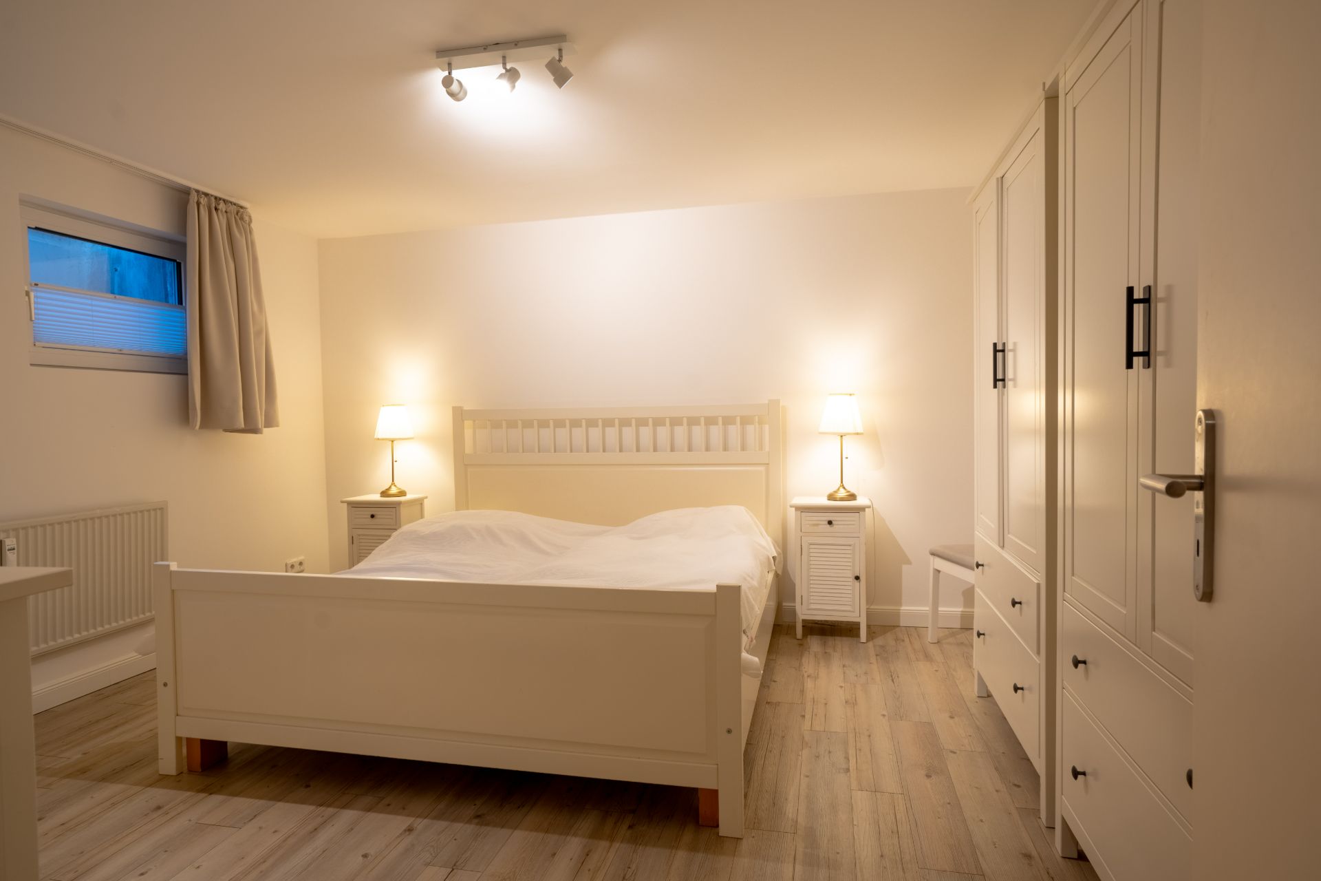 Helles Schlafzimmer mit Doppelbett, zwei Nachttischen, Stehlampen und großem Kleiderschrank.
