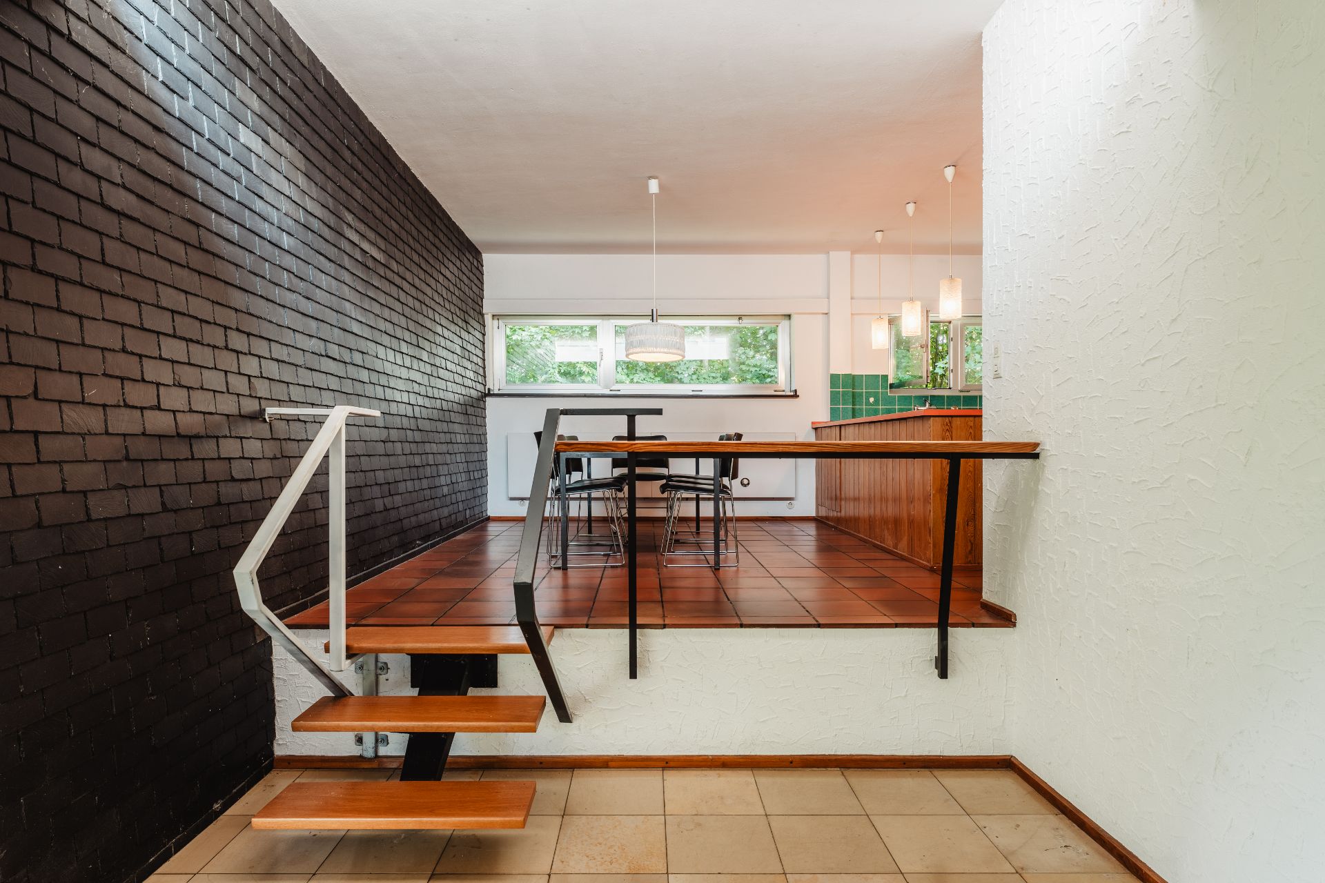 Offene Küche und Essbereich mit brauner Wand und Holzstufen, große Fenster im Hintergrund.