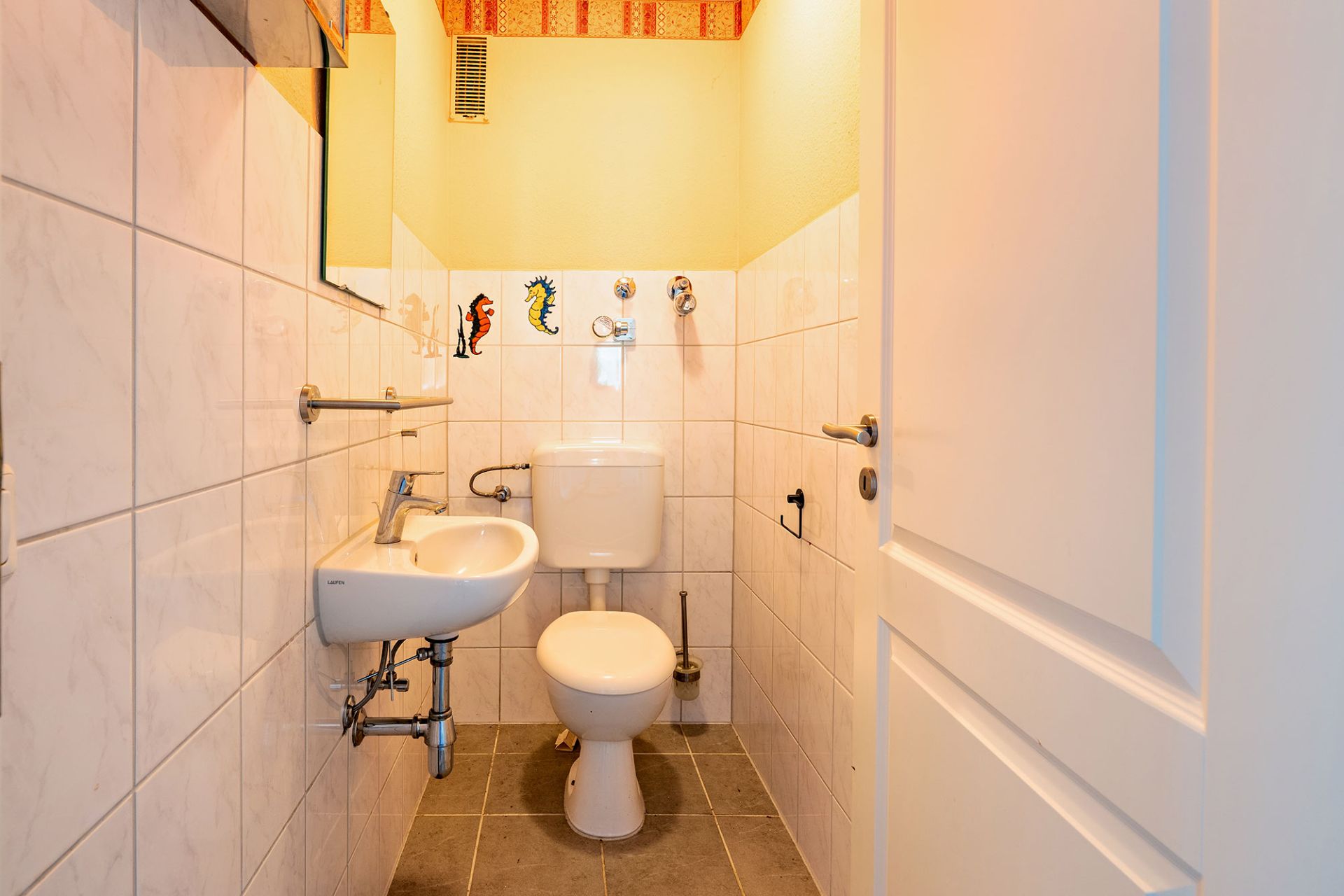 Kleines Badezimmer mit Toilette, Waschbecken und weiß gefliesten Wänden.