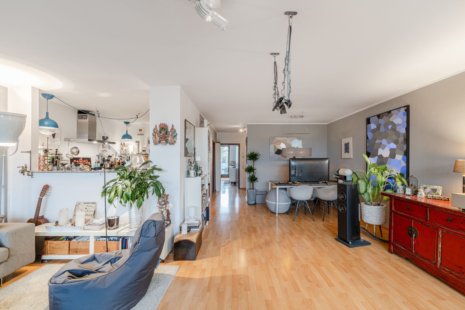 Helles Wohnzimmer mit Holzfußboden, Pflanzen, Schreibtisch, Regalen und Kunst an den Wänden.