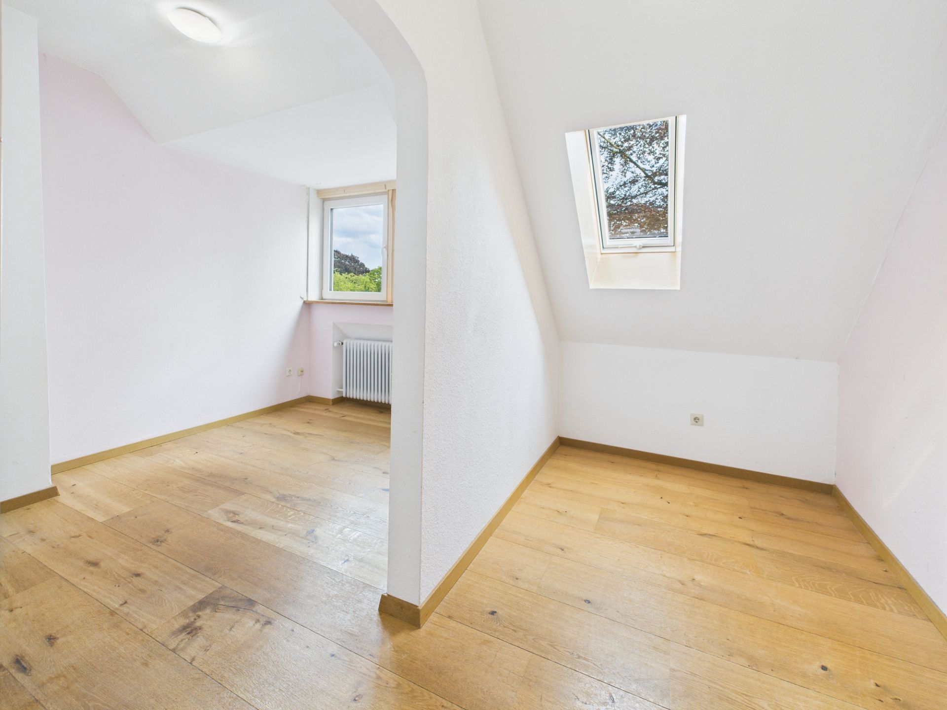 Leerer Raum mit Holzfußboden, Dachfenster und normalem Fenster, geteilt durch einen Rundbogen.