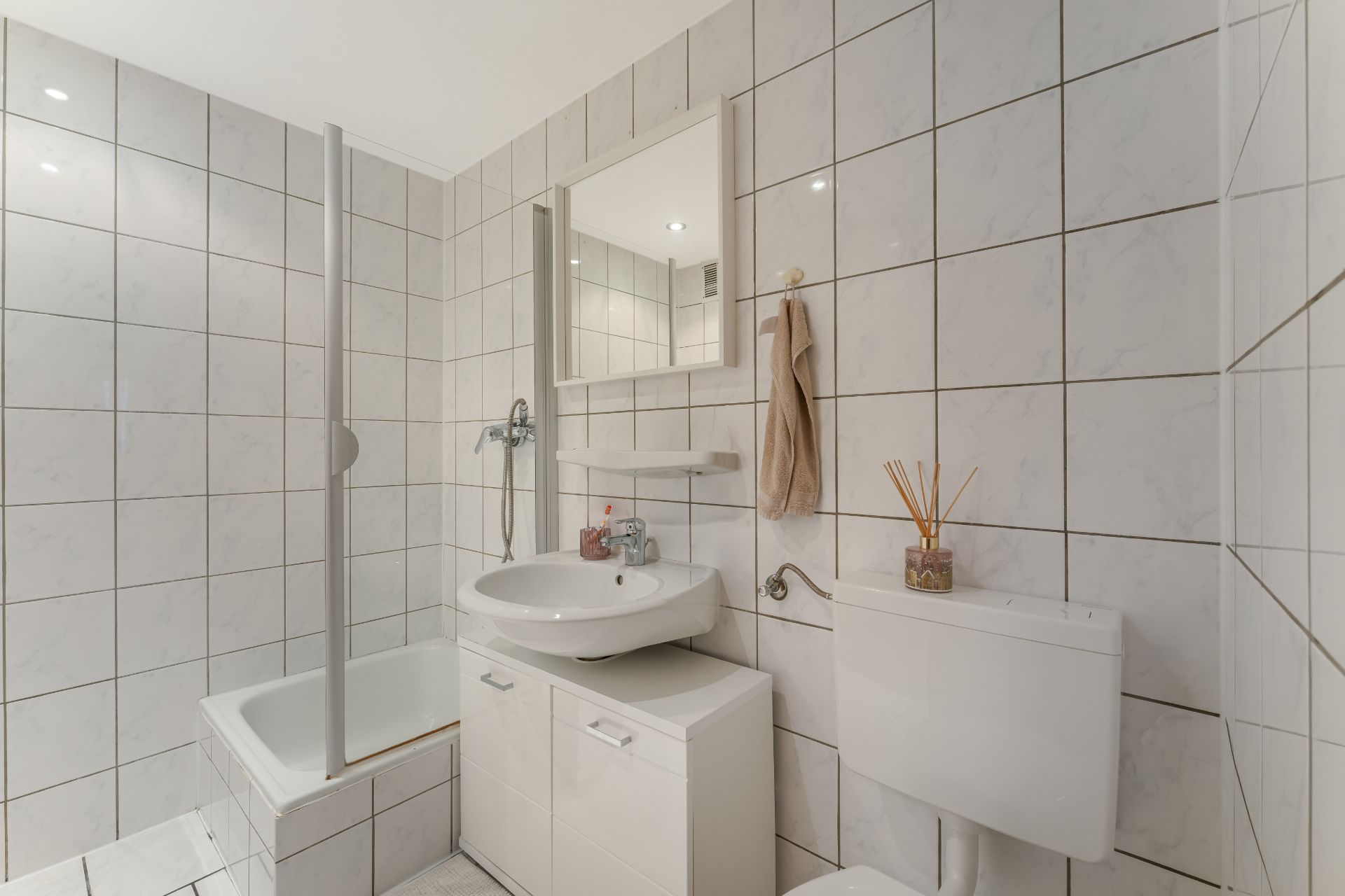 Helles Badezimmer mit Badewanne, Waschbecken, Spiegel und Toilette, alles mit weißen Fliesen.
