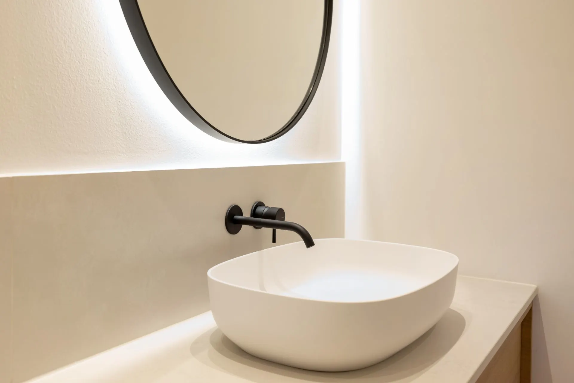 Modernes Badezimmer mit rundem Spiegel und weißem Waschbecken auf einer hellen Arbeitsplatte.