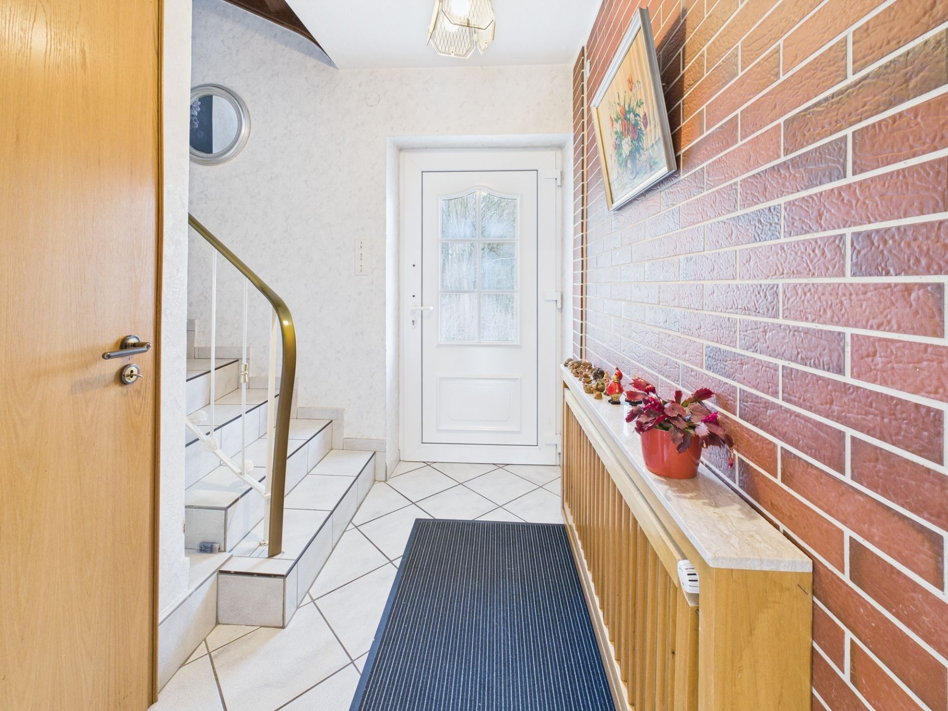 Heller Flur mit weißer Tür, gemusterter Wand, Treppe und rotem Ziegelwandelement.