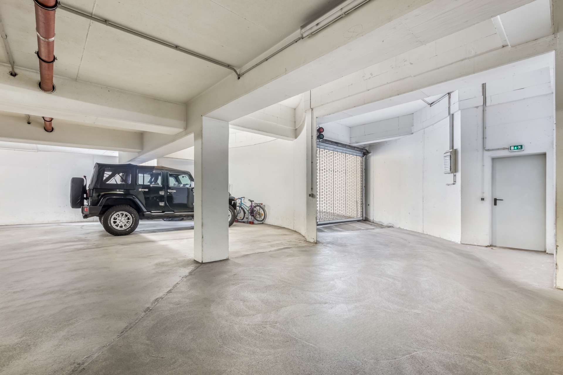 Helle Tiefgarage mit einem schwarzen Auto, zwei Fahrrädern und einem offenen Tor.