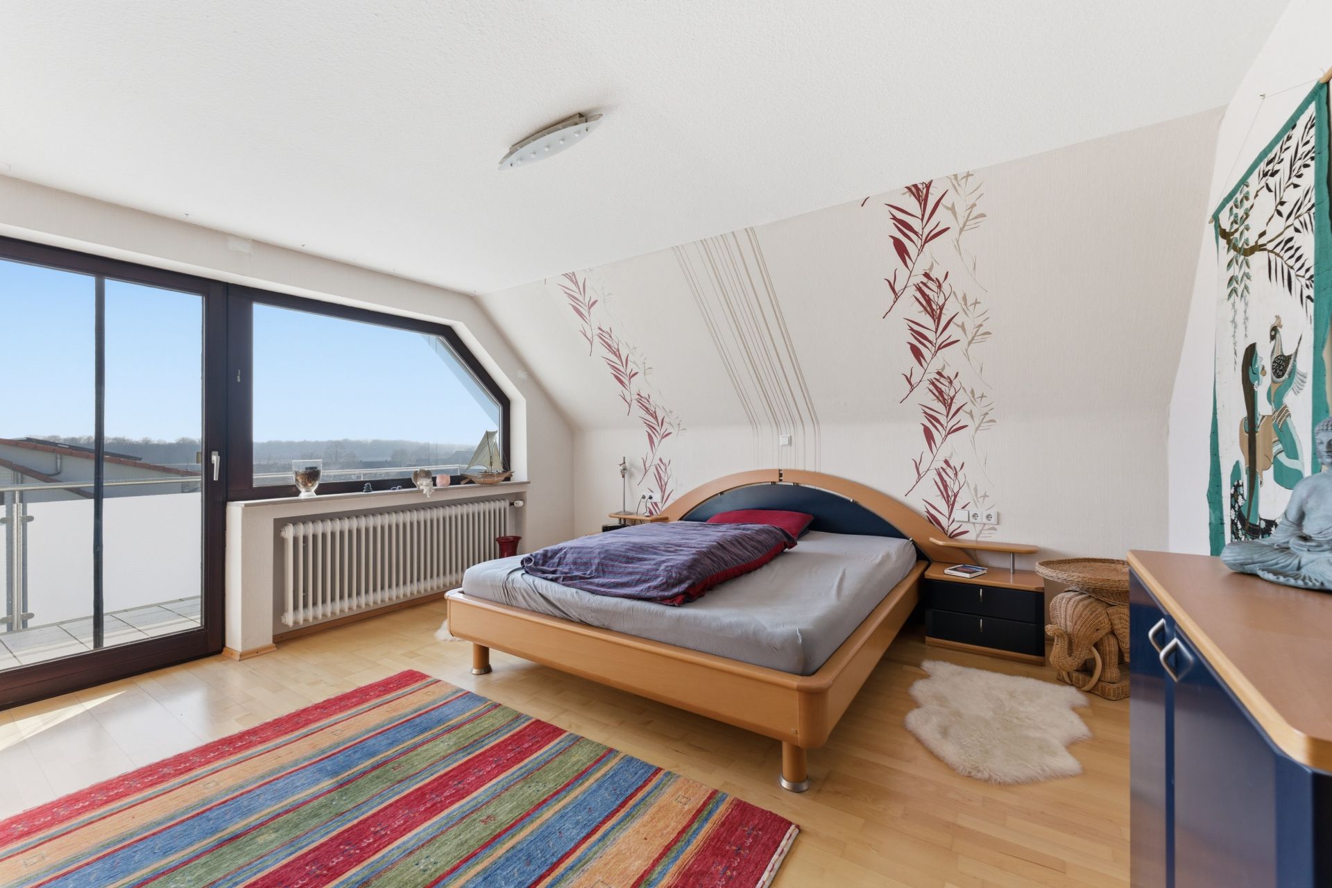 Helles Schlafzimmer mit Doppelbett, buntem Teppich und Balkonzugang.