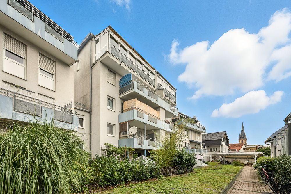 Mehrfamilienhaus mit Balkonen und Grünanlage an einem sonnigen Tag.