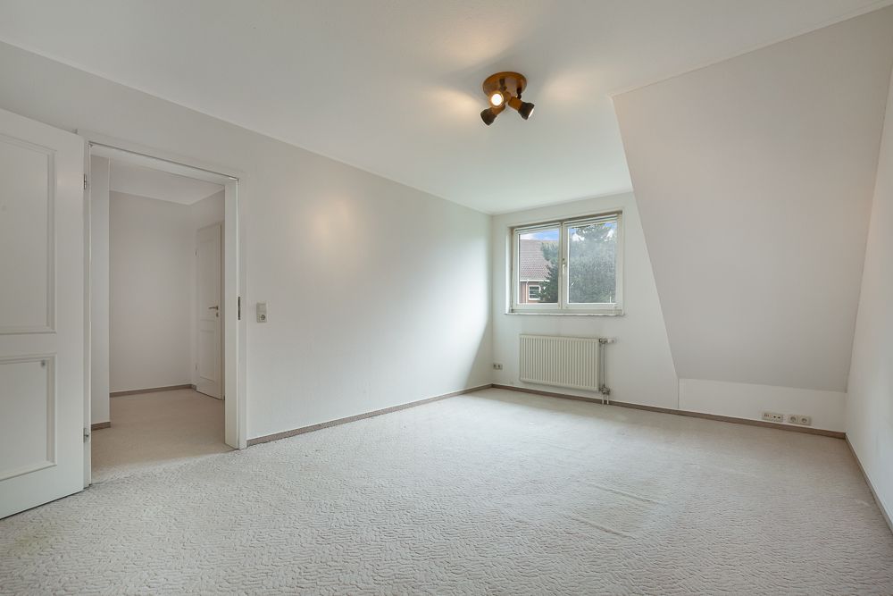 Leeres, helles Zimmer mit Teppichboden, Fenster und Heizung an der Wand.