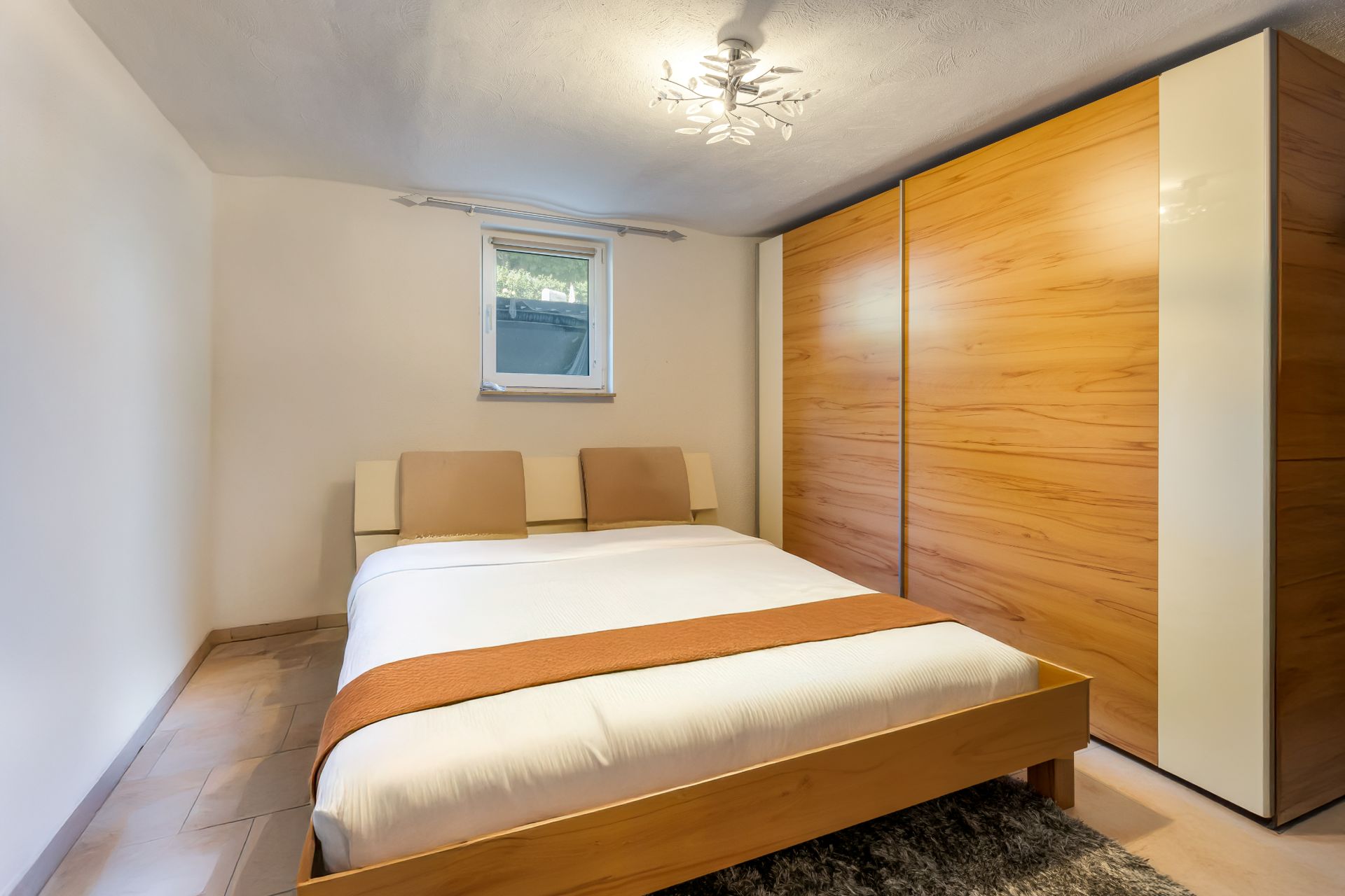 Schlafzimmer mit Doppelbett, großem Holzschrank und Fenster, helle Wände und Decke.