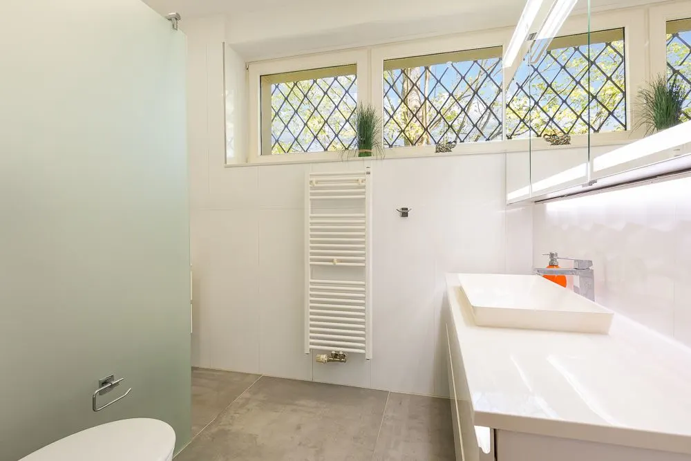 Modernes Badezimmer mit großem Fenster, Heizkörper, Waschbecken und Spiegel.