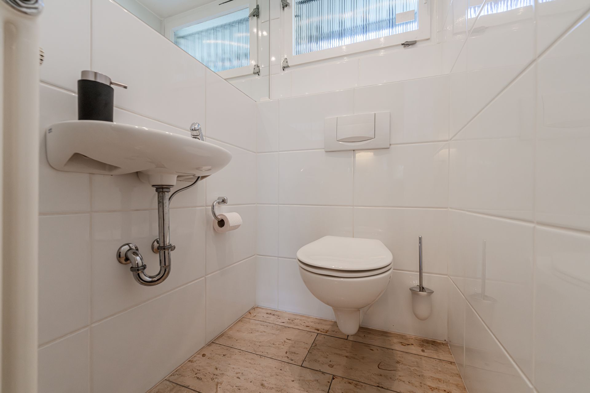 Kleines Badezimmer mit Wandtoilette, kleinem Waschbecken und einem Fenster.