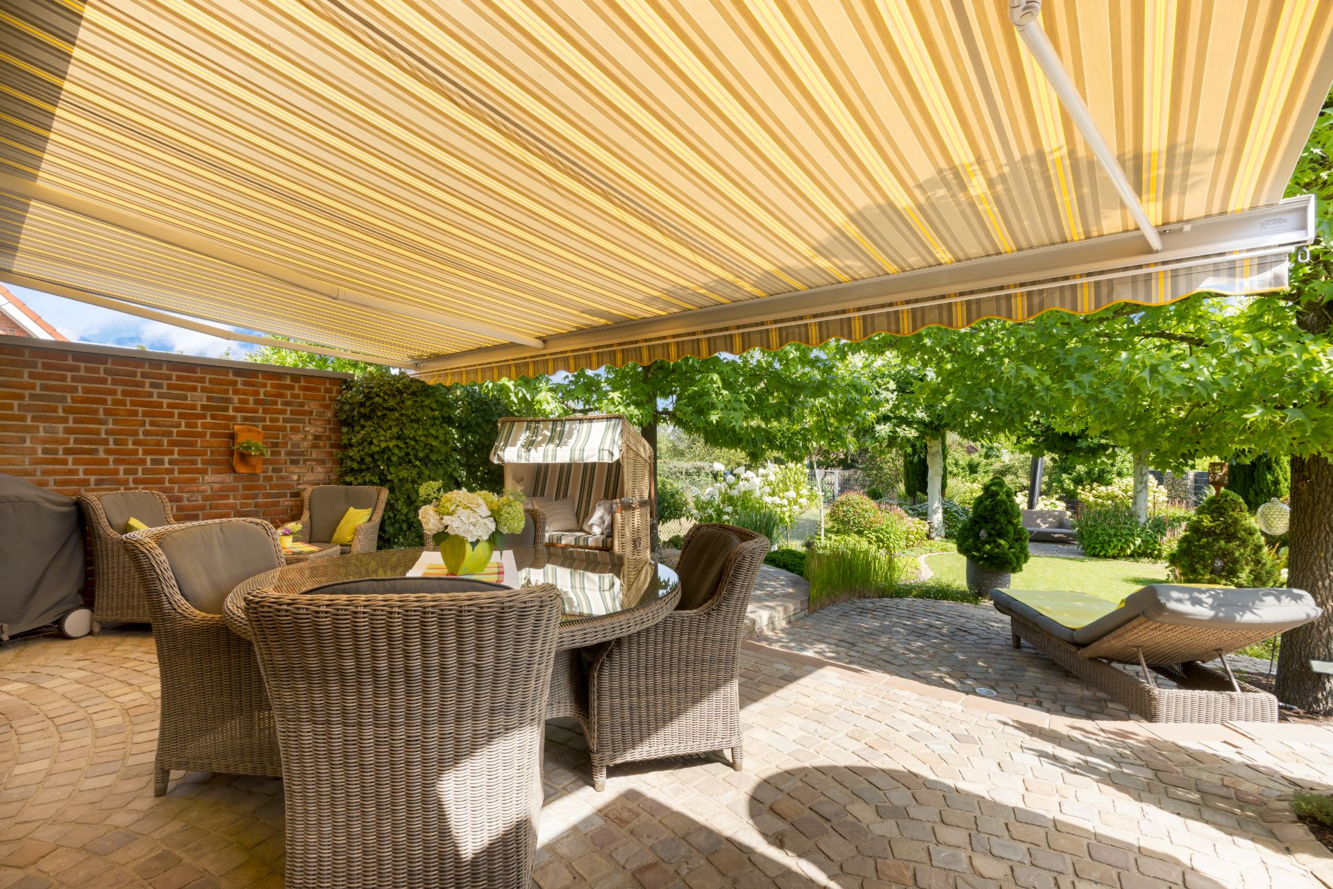 Terrasse mit Korbmöbeln, gelber Markise und Blick auf einen grünen Garten.