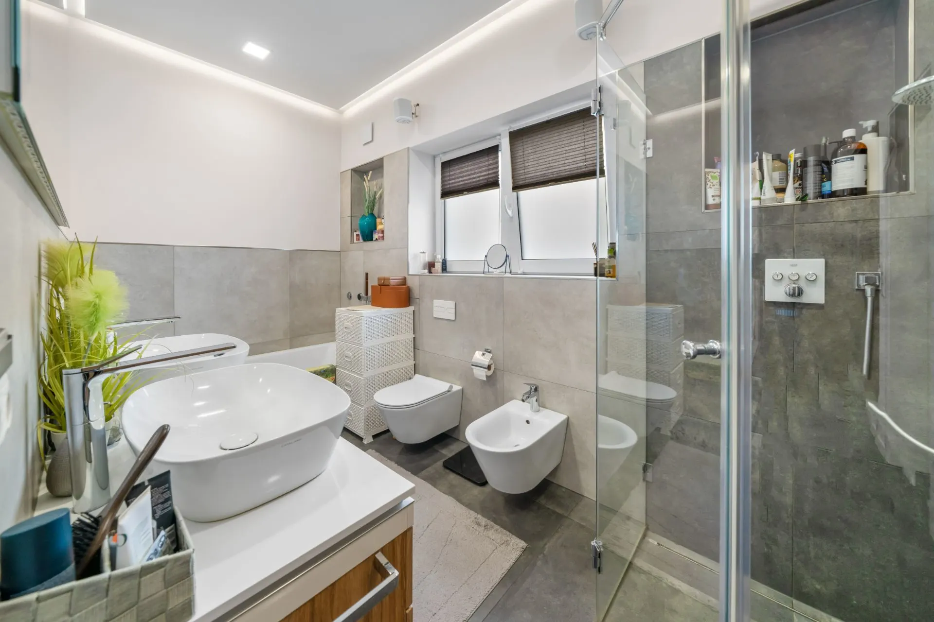 Modernes Badezimmer mit Waschbecken, Dusche, WC, Bidet und großem Fenster.