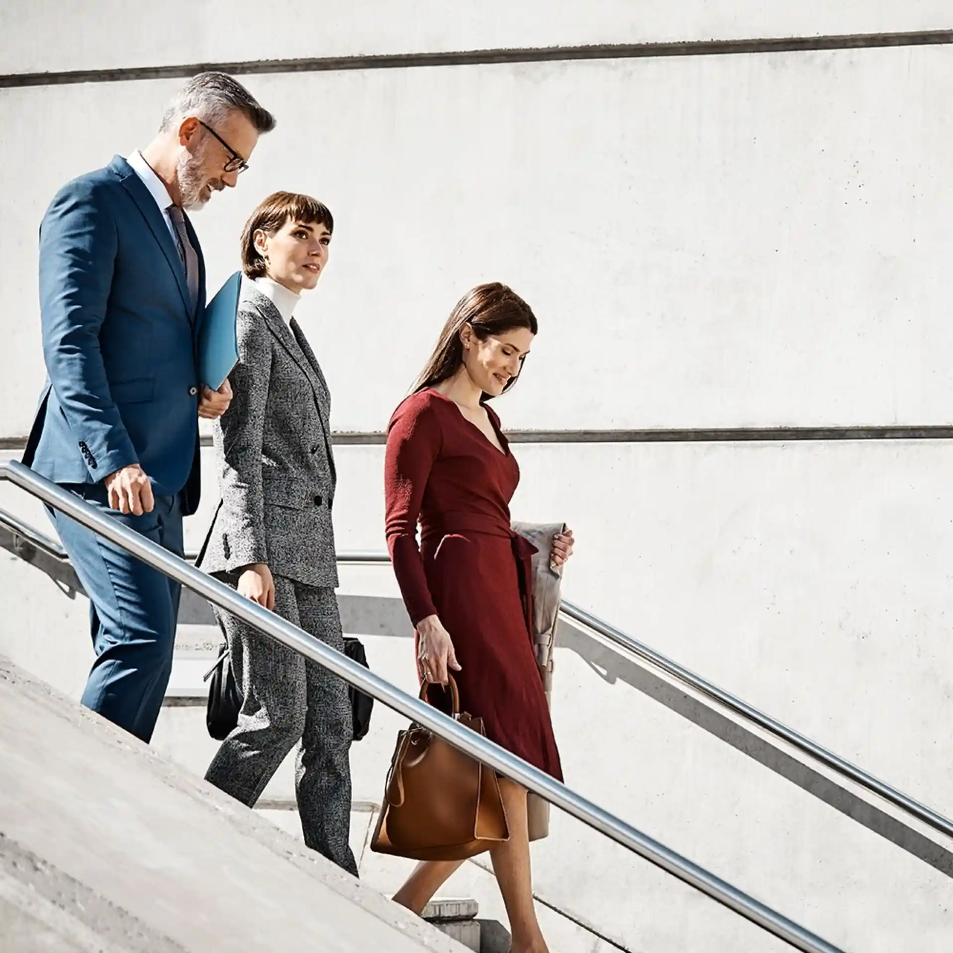 Drei Personen gehen zusammen eine Treppe entlang, vor einer Betonwand.