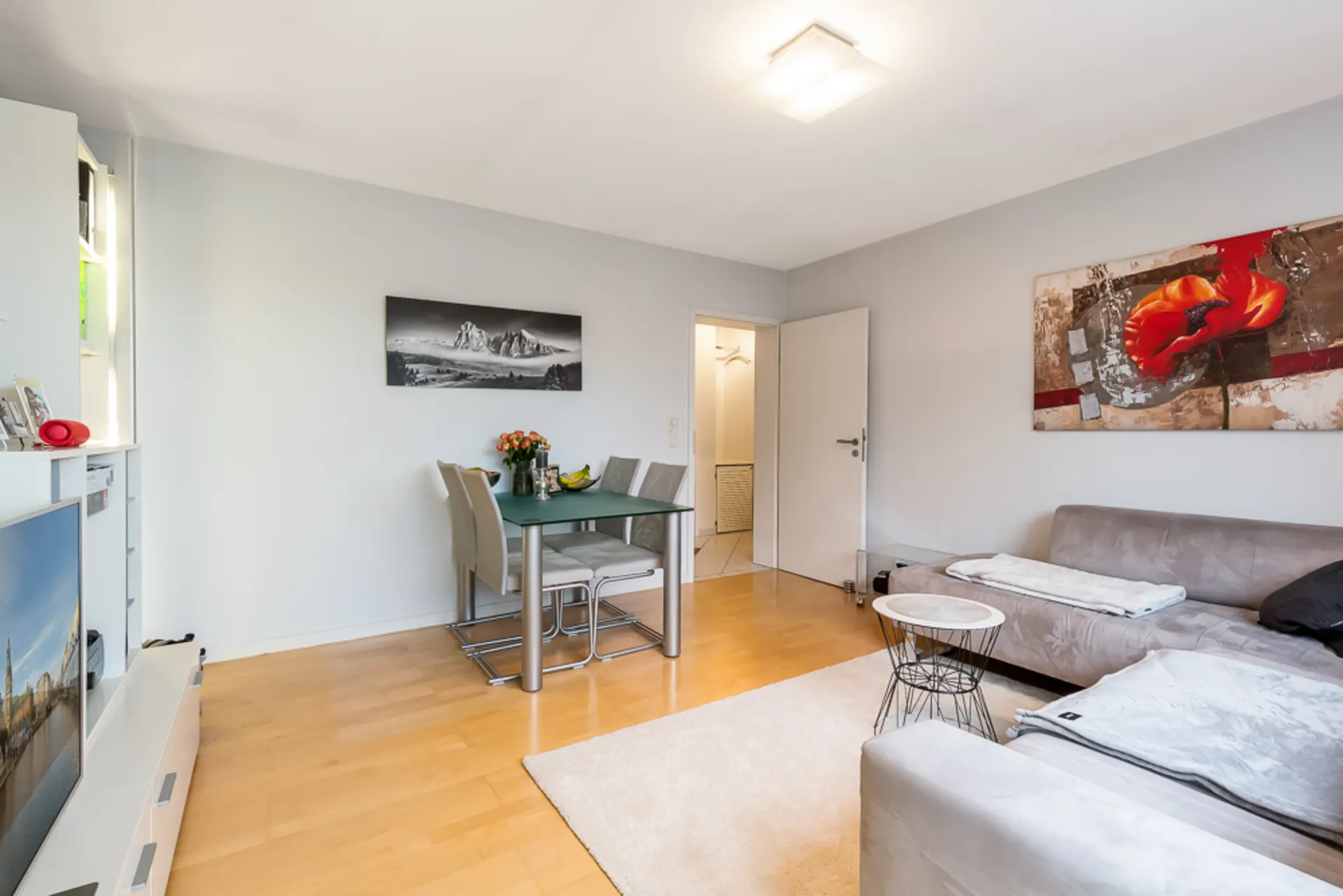 Wohnzimmer mit grauem Sofa, Esstisch mit vier Stühlen und moderner Wandkunst.