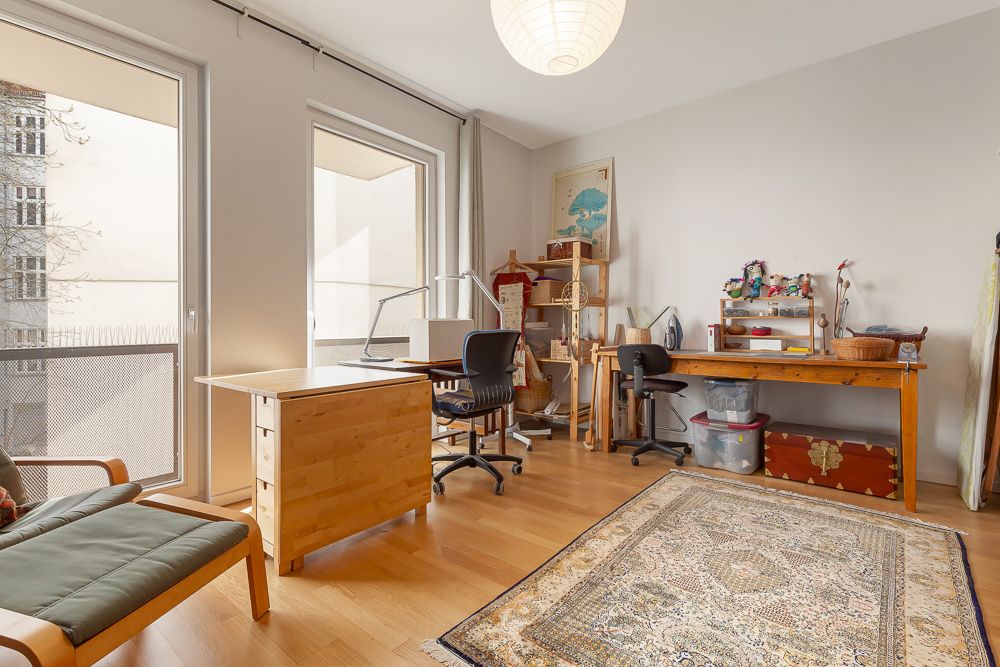 Helles Arbeitszimmer mit zwei Schreibtischen, Regal, Teppich und Balkonzugang.