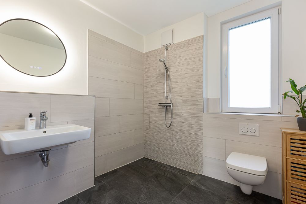 Modernes Badezimmer mit Dusche, Wandwaschbecken, WC und Fenster.