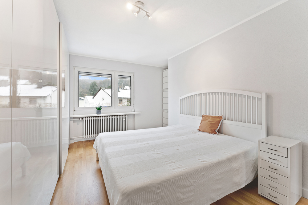 Helles Schlafzimmer mit Doppelbett, Nachttisch, Kleiderschrank und zwei Fenstern.