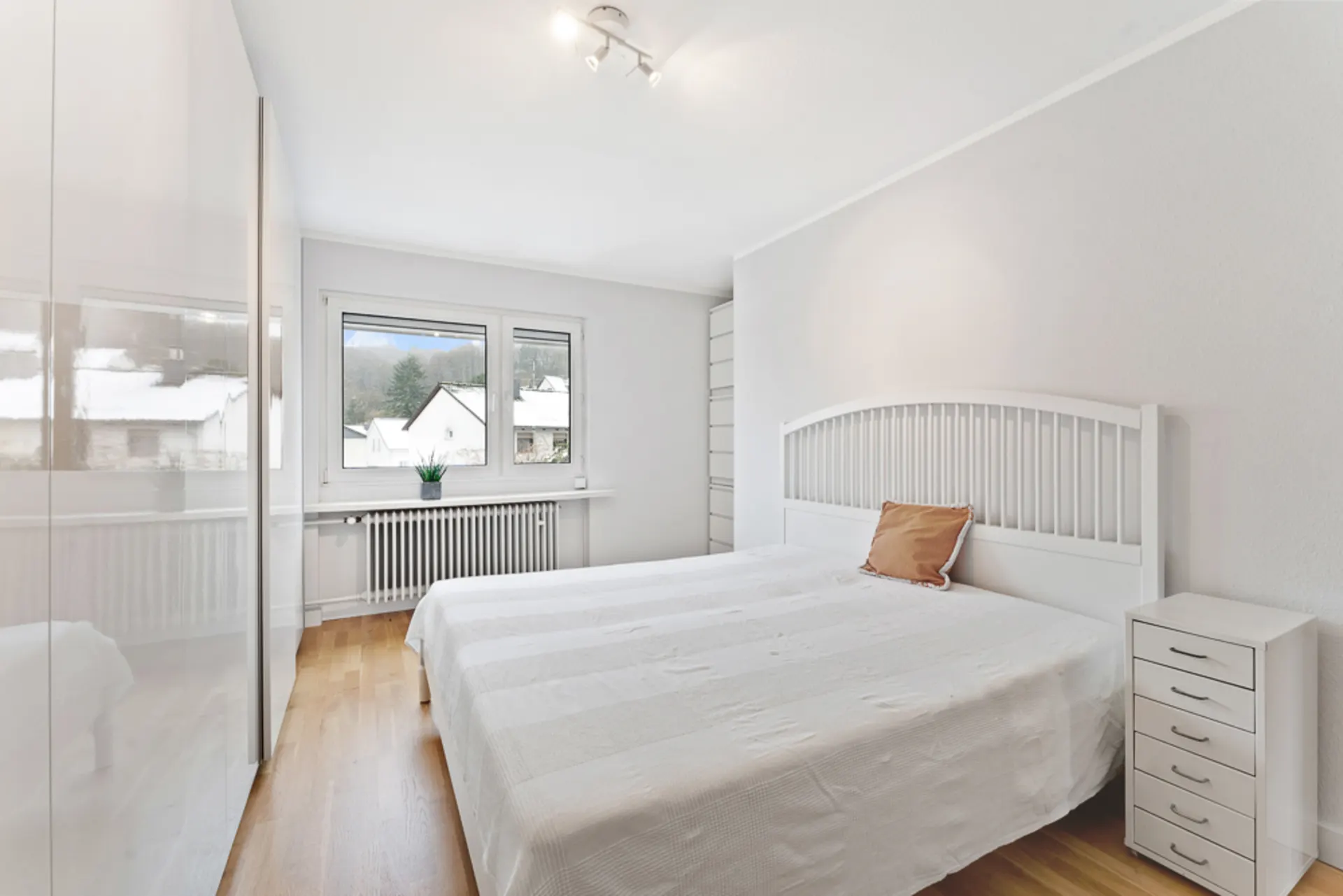 Helles Schlafzimmer mit Doppelbett, Nachttisch, Kleiderschrank und zwei Fenstern.