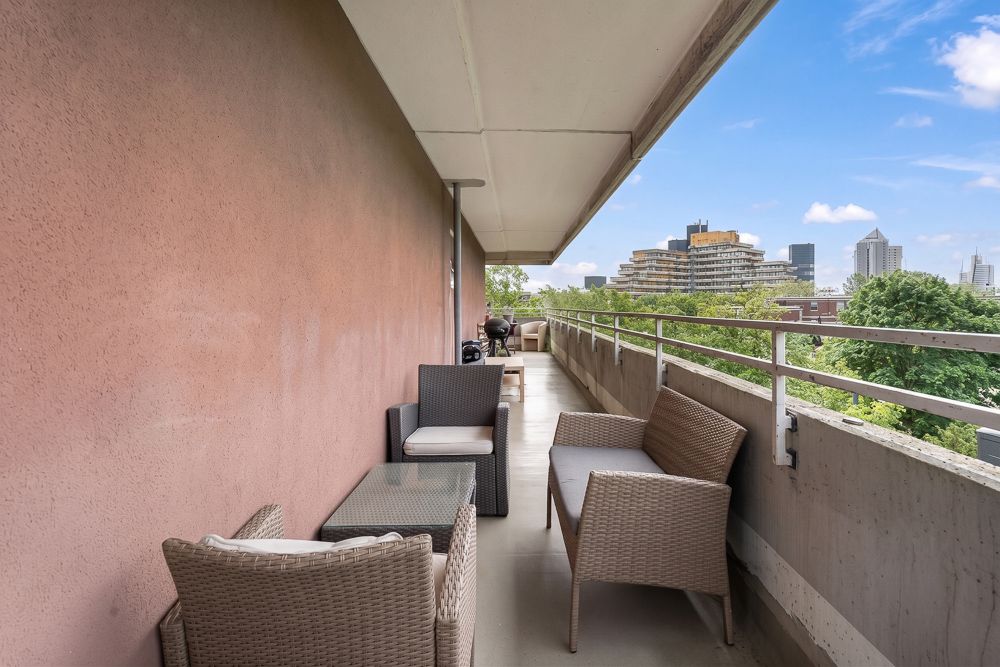 Langer Balkon mit Sitzmöbeln und Blick auf Bäume und Stadtgebäude.
