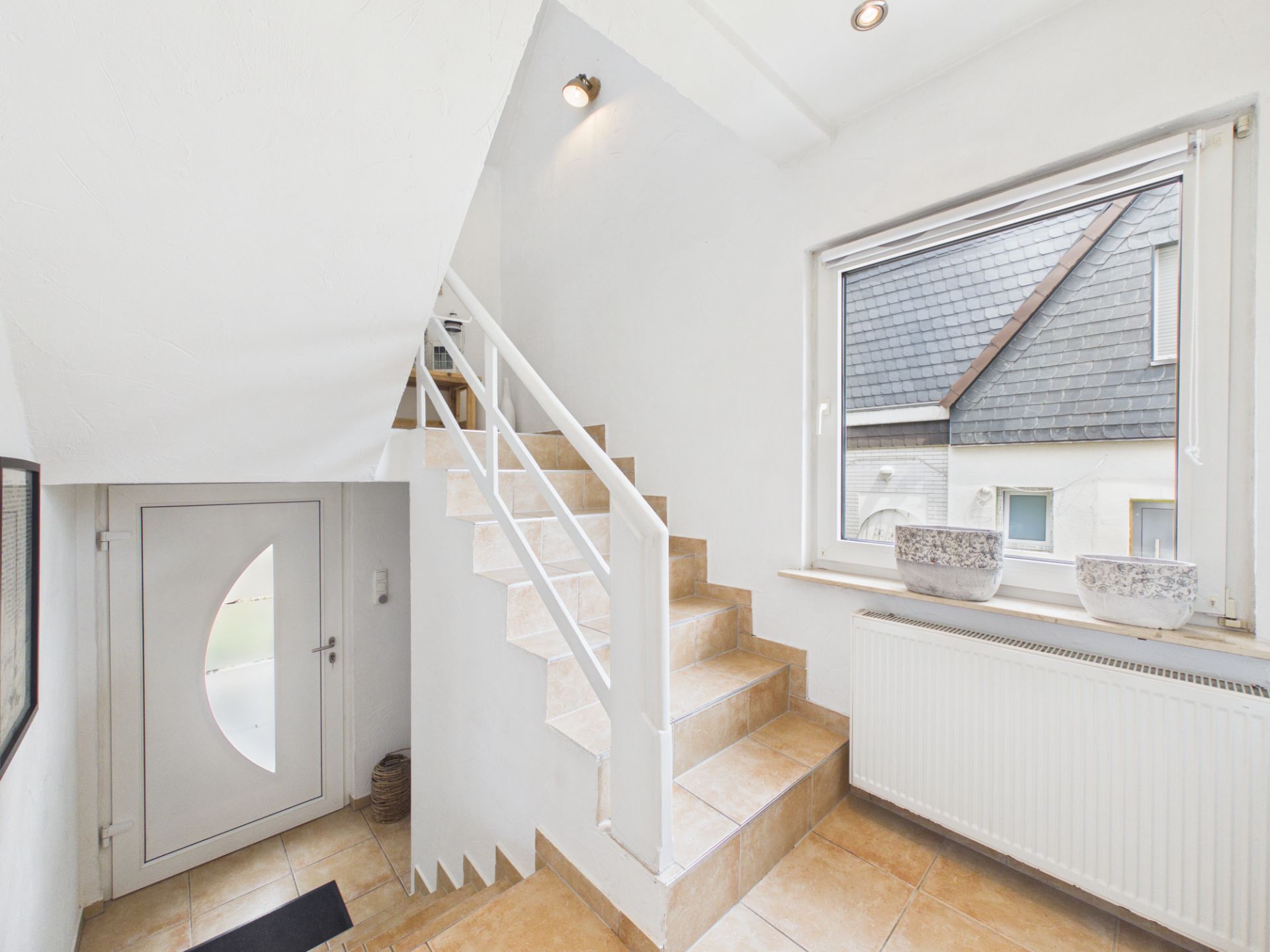 Heller Flur mit Treppe, Fenster, Heizkörper und weißer Haustür.