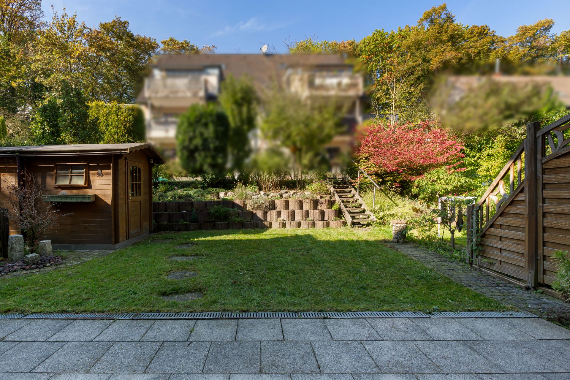 Garten mit Rasenfläche, Holzschuppen und Treppe, von Terrasse aus gesehen.