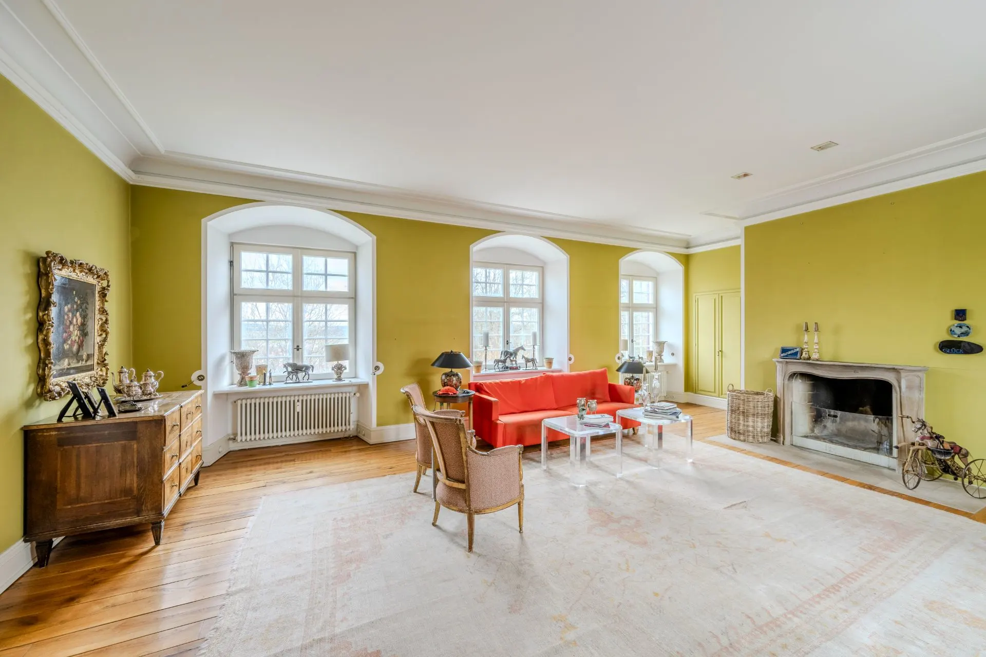 Helles Wohnzimmer mit roten Sofa, Kamin, drei Fenstern und Holzfußboden.