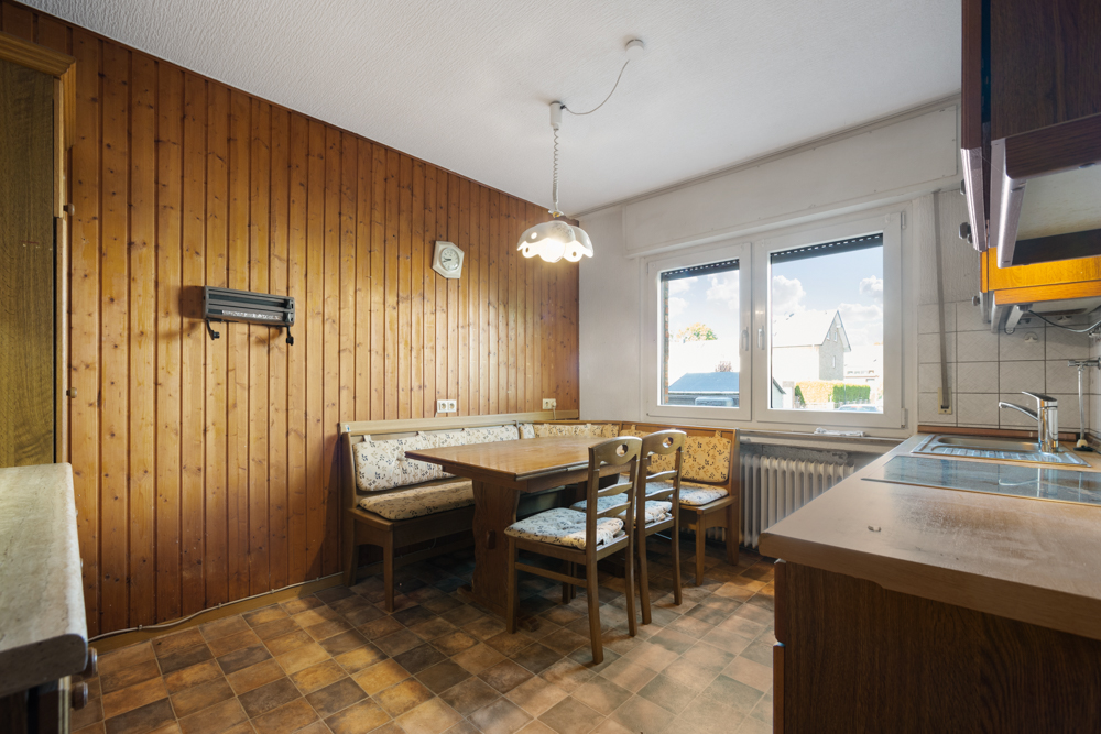 Küche mit Holzwand, Eckbank, Esstisch, Stühlen und zwei großen Fenstern.