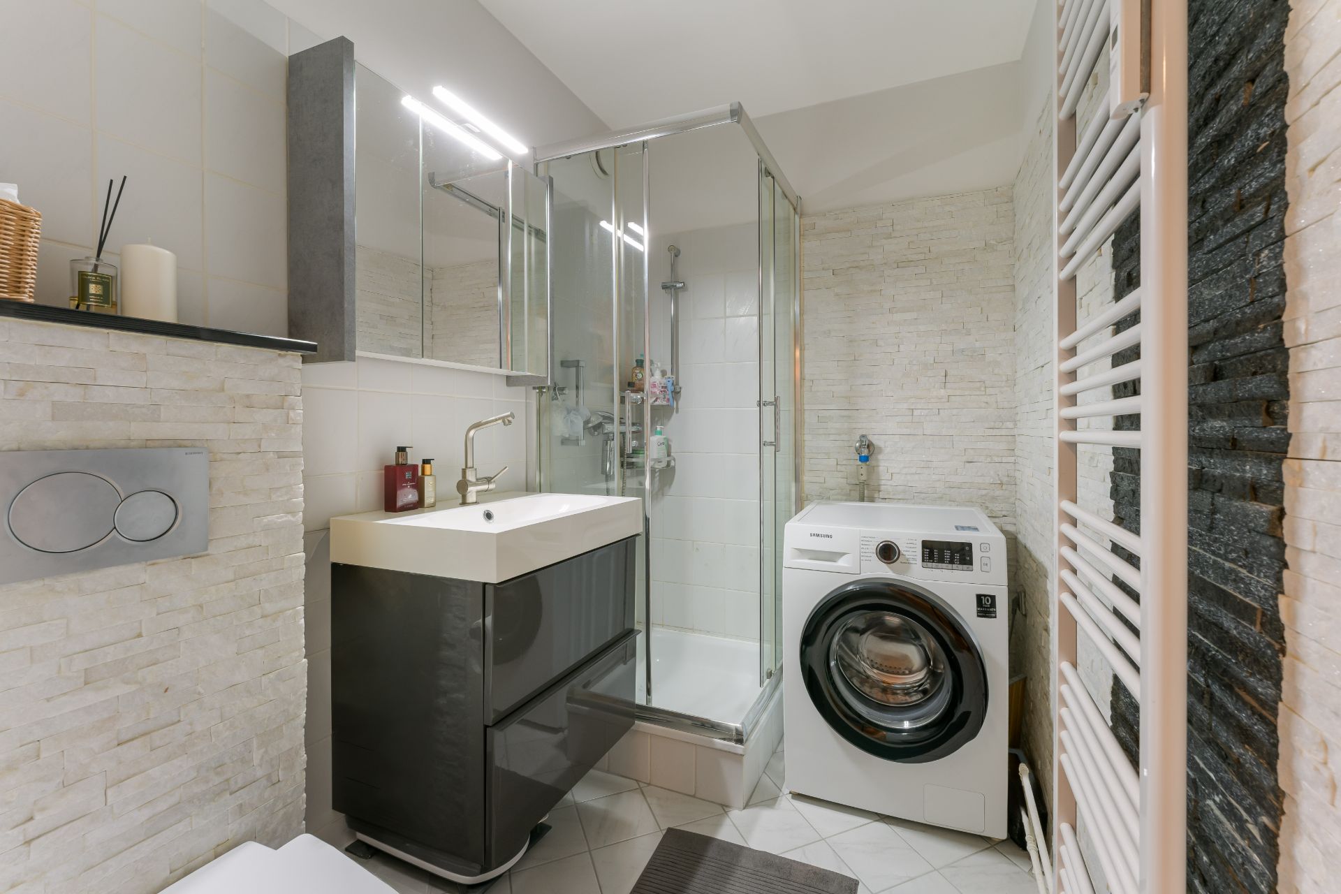 Modernes Badezimmer mit Waschmaschine, Dusche, Waschbecken und Handtuchheizkörper.