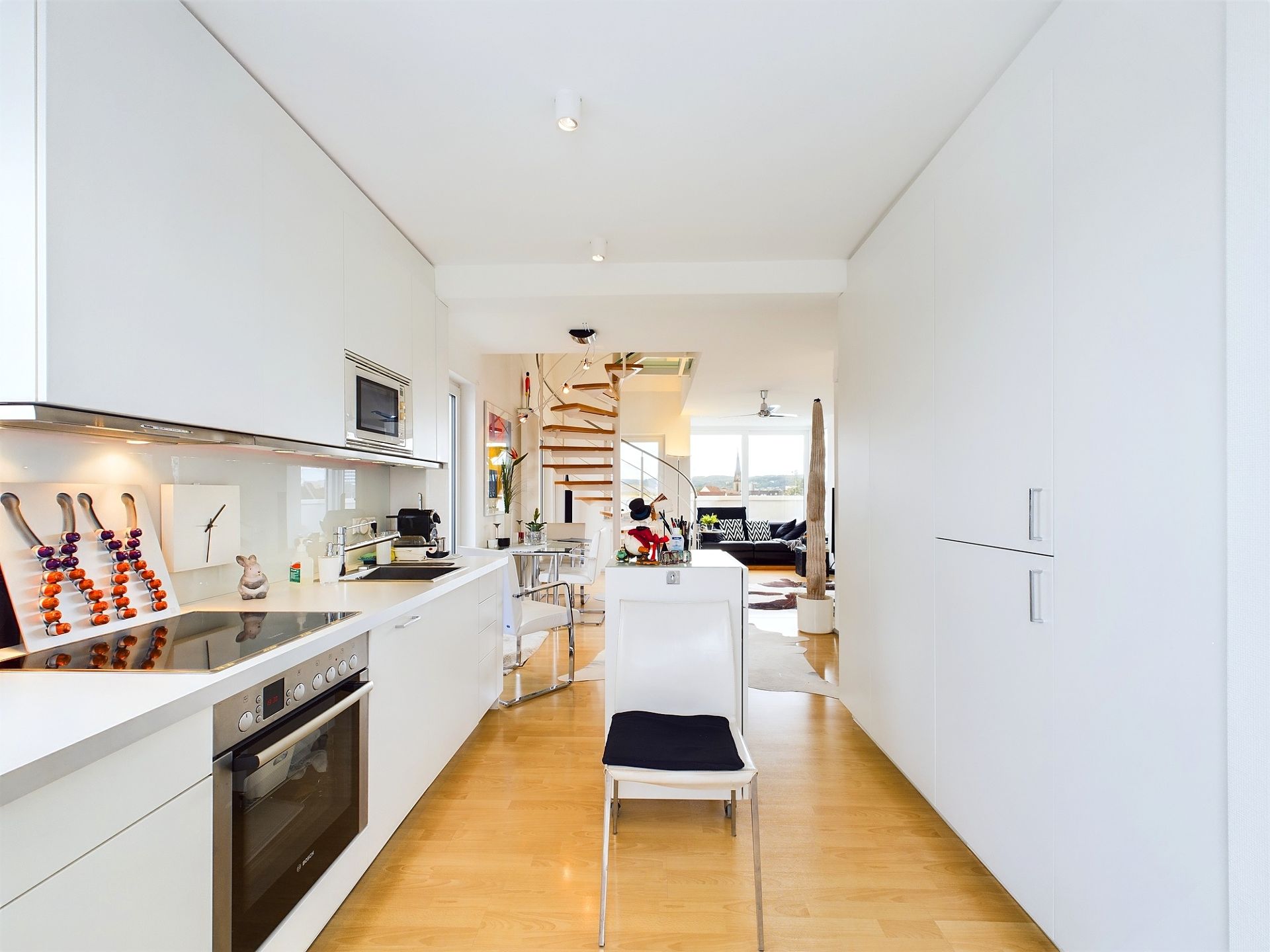Helle, moderne Küche mit weißen Schränken, Holzfußboden und einer offenen Treppe im Hintergrund.