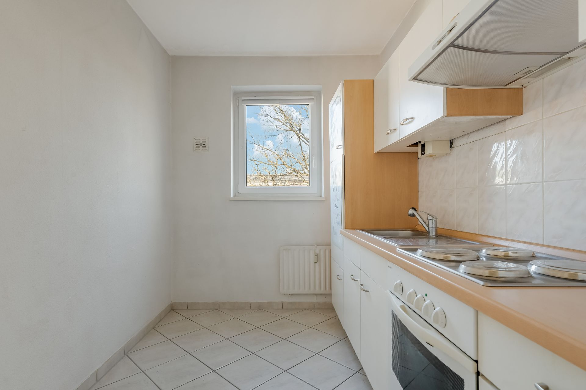 Schmale Einbauküche mit weißen Schränken, Herd, Spüle und Fenster.