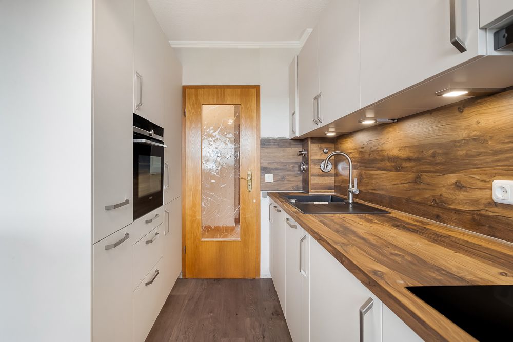 Moderne Einbauküche mit Holzarbeitsplatte, Spüle, Herd und Backofen, Tür im Hintergrund.